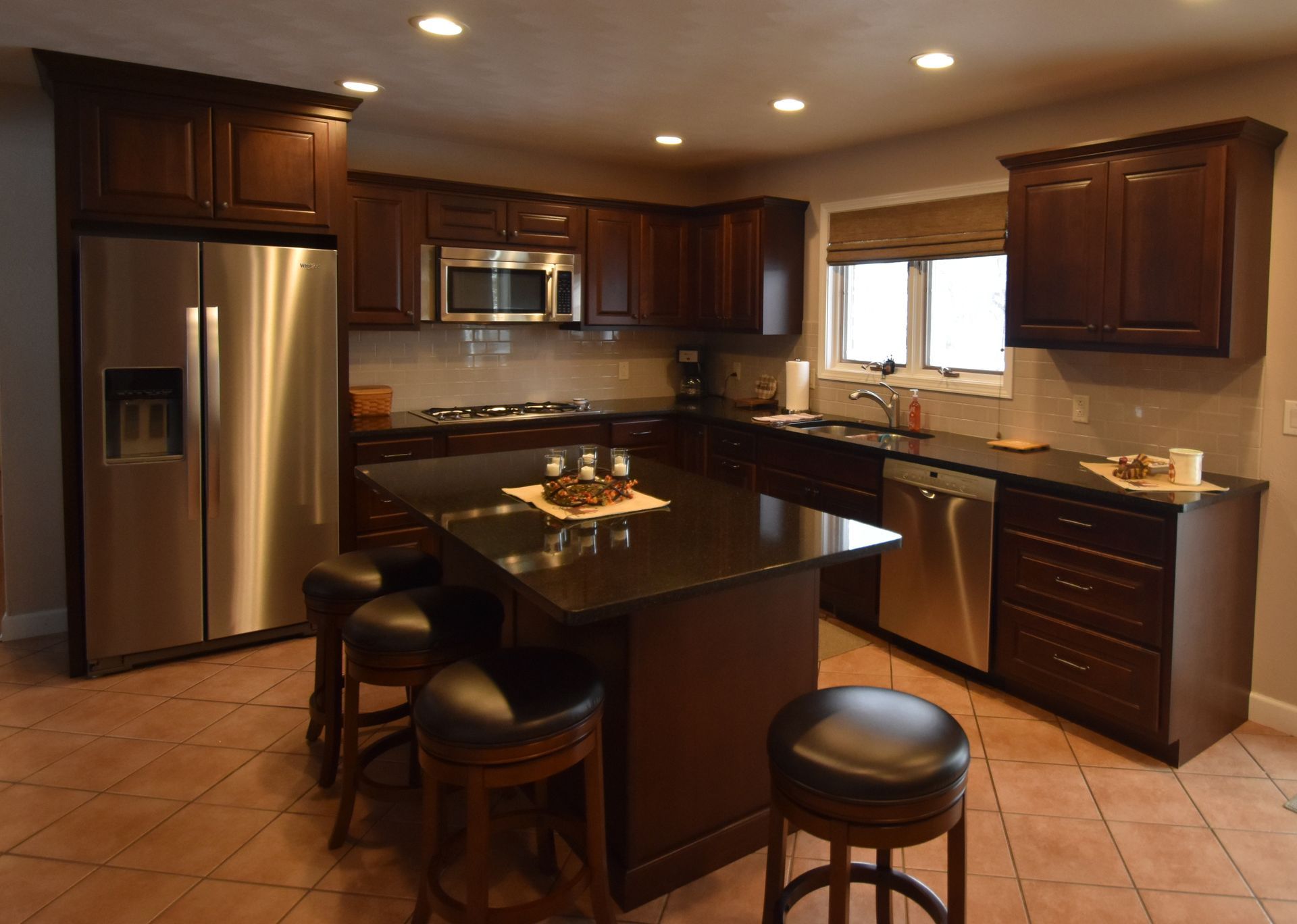 Modern kitchen with stainless steel appliances, dark wood cabinets, and a central island with stools.
