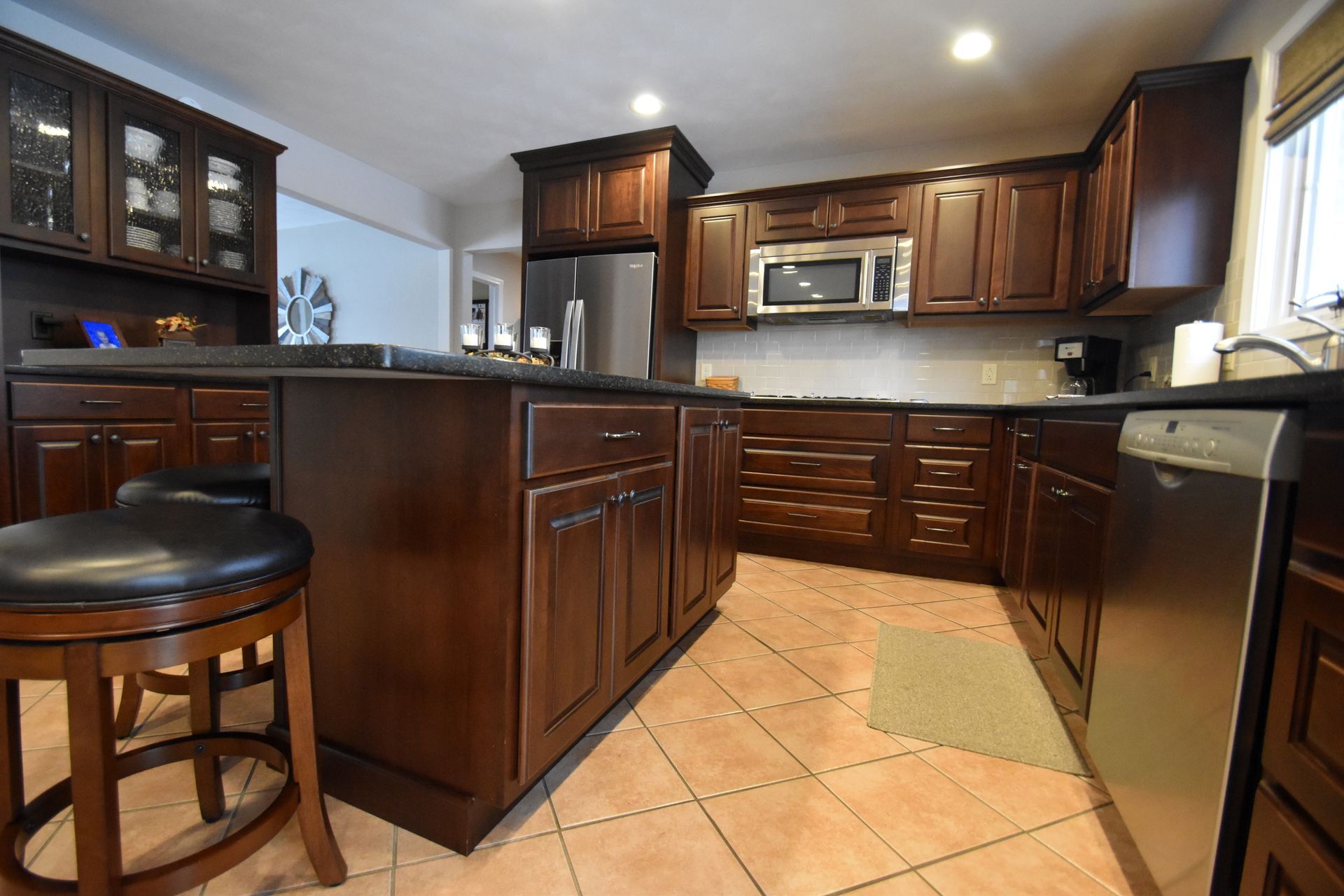 Dark wood kitchen with island, tile floor, stainless appliances, and two stools in a bright, modern interior