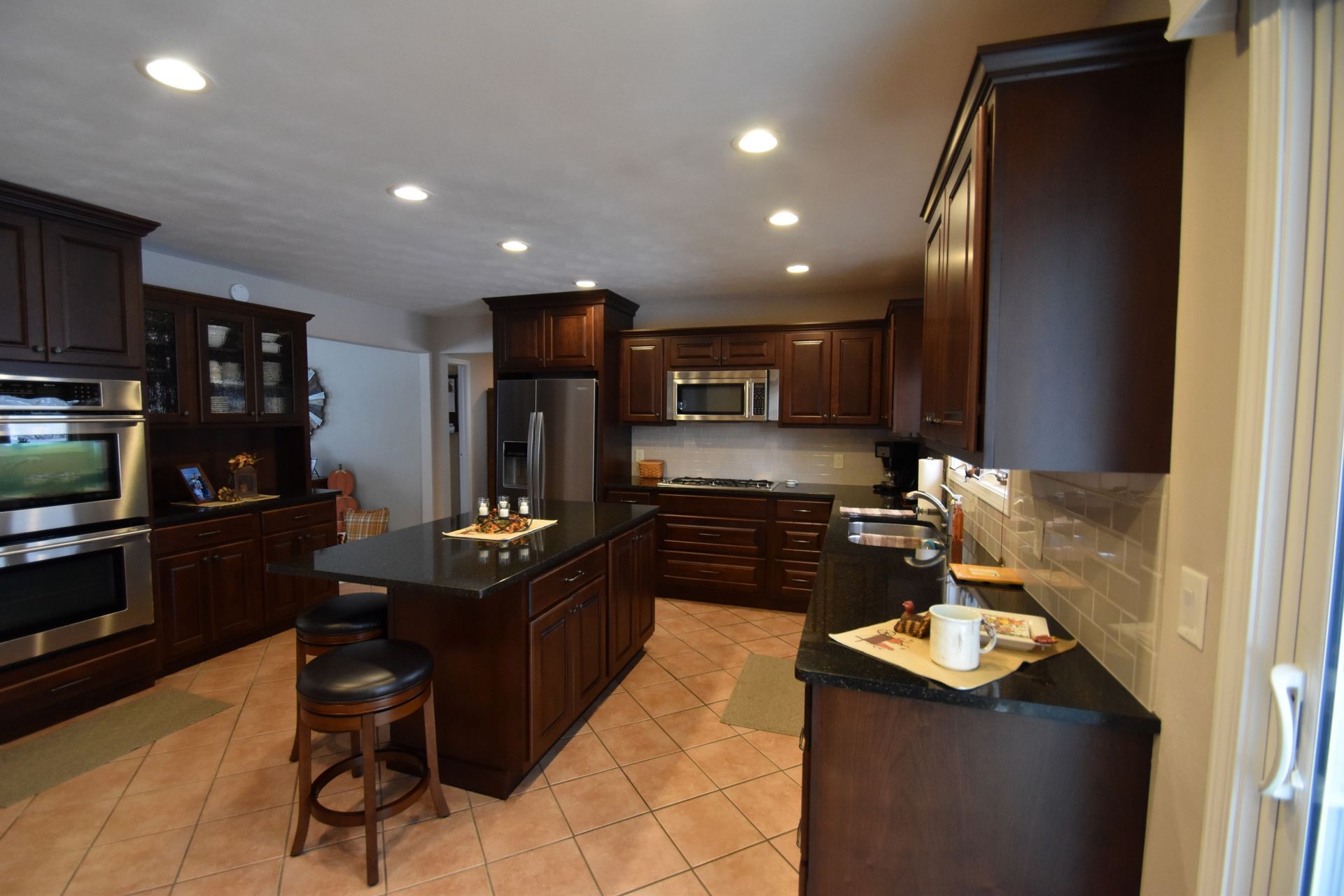 Modern kitchen with dark wood cabinets, black island, stainless appliances, and tiled floor