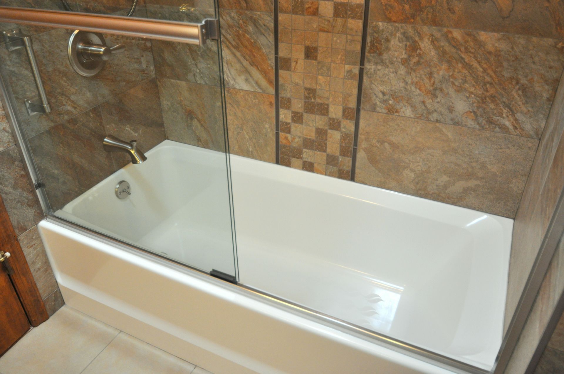 Modern white bathtub with glass shower screen and tiled wall in a bathroom