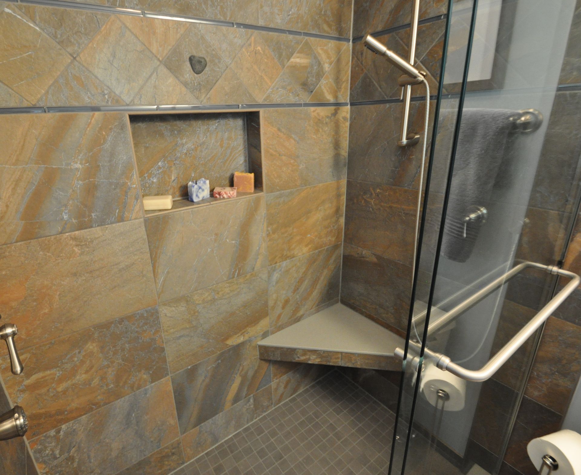 Walk-in shower with tiled walls, built-in shelf, glass door, and a corner bench seat.