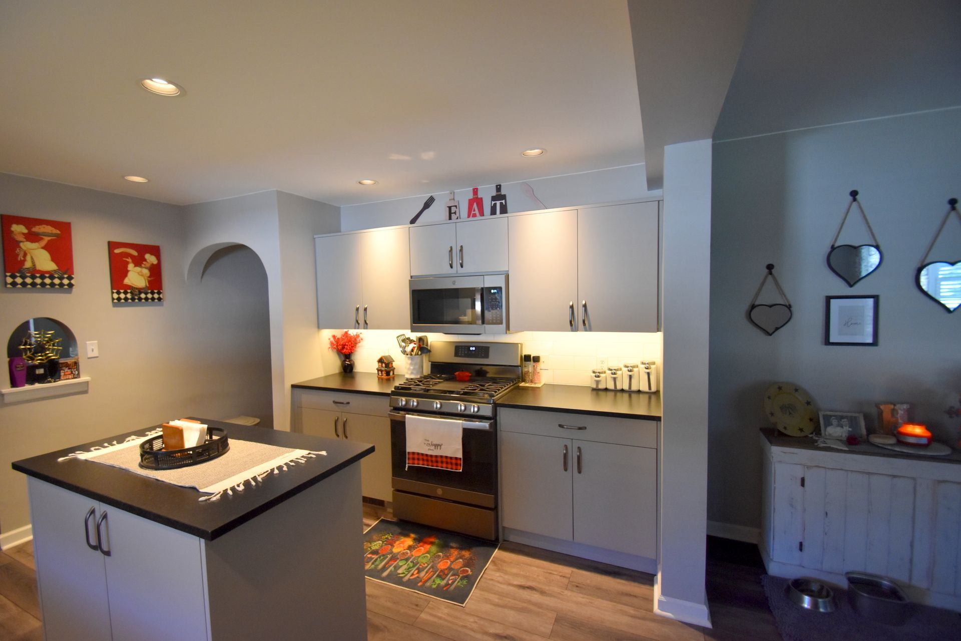 Bright modern kitchen with island, stainless steel appliances, gray cabinets, and warm under-cabinet lighting.