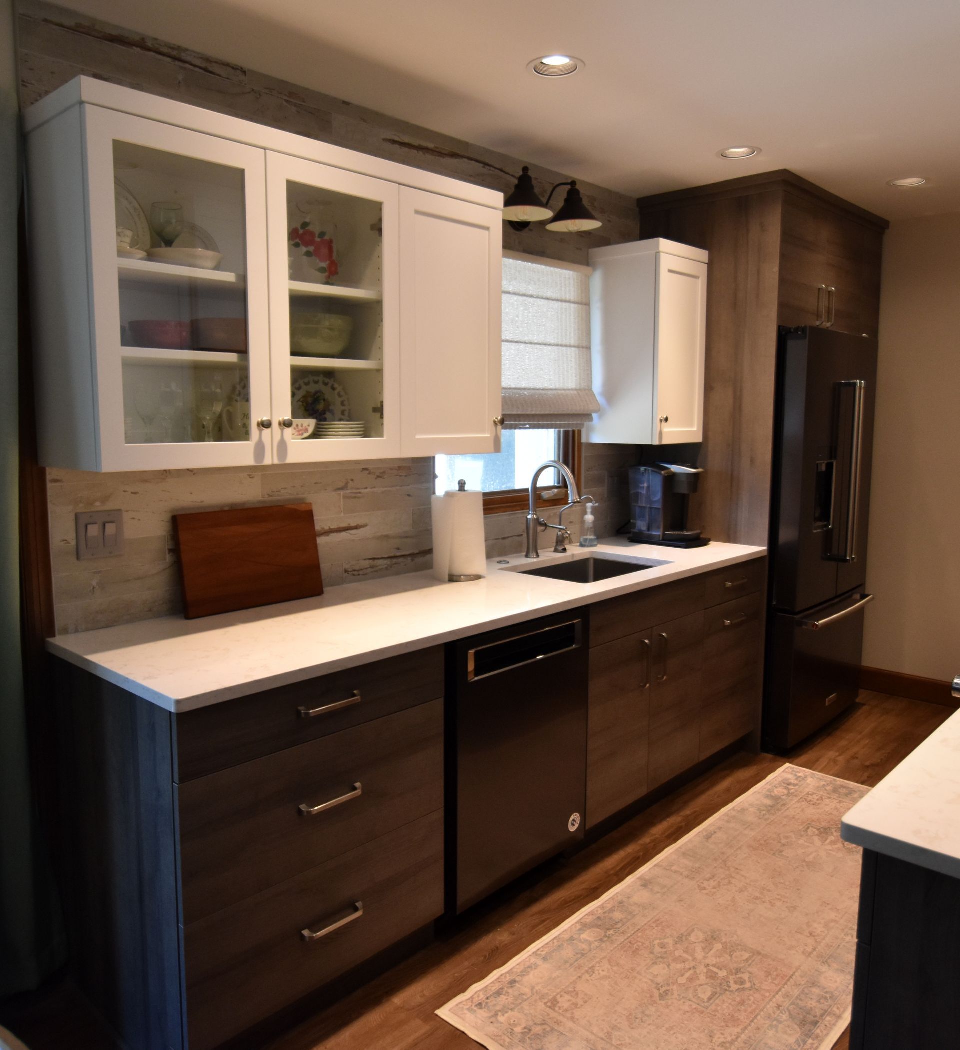 Modern kitchen with white cabinets, dark wood lower cabinets, stainless appliances, and a light countertop.