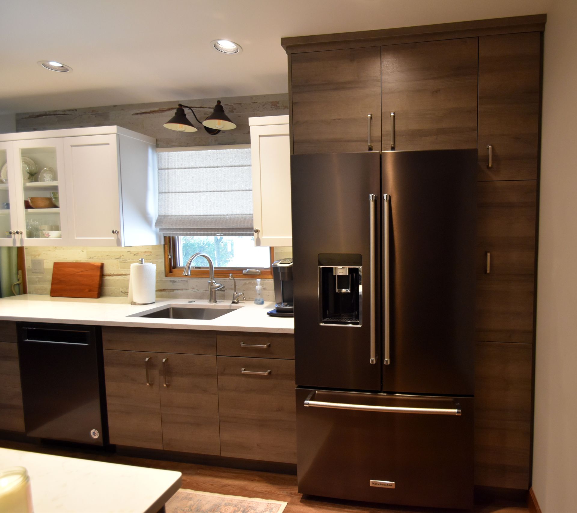 Modern kitchen with white cabinets, dark wood island, and stainless steel fridge and dishwasher.
