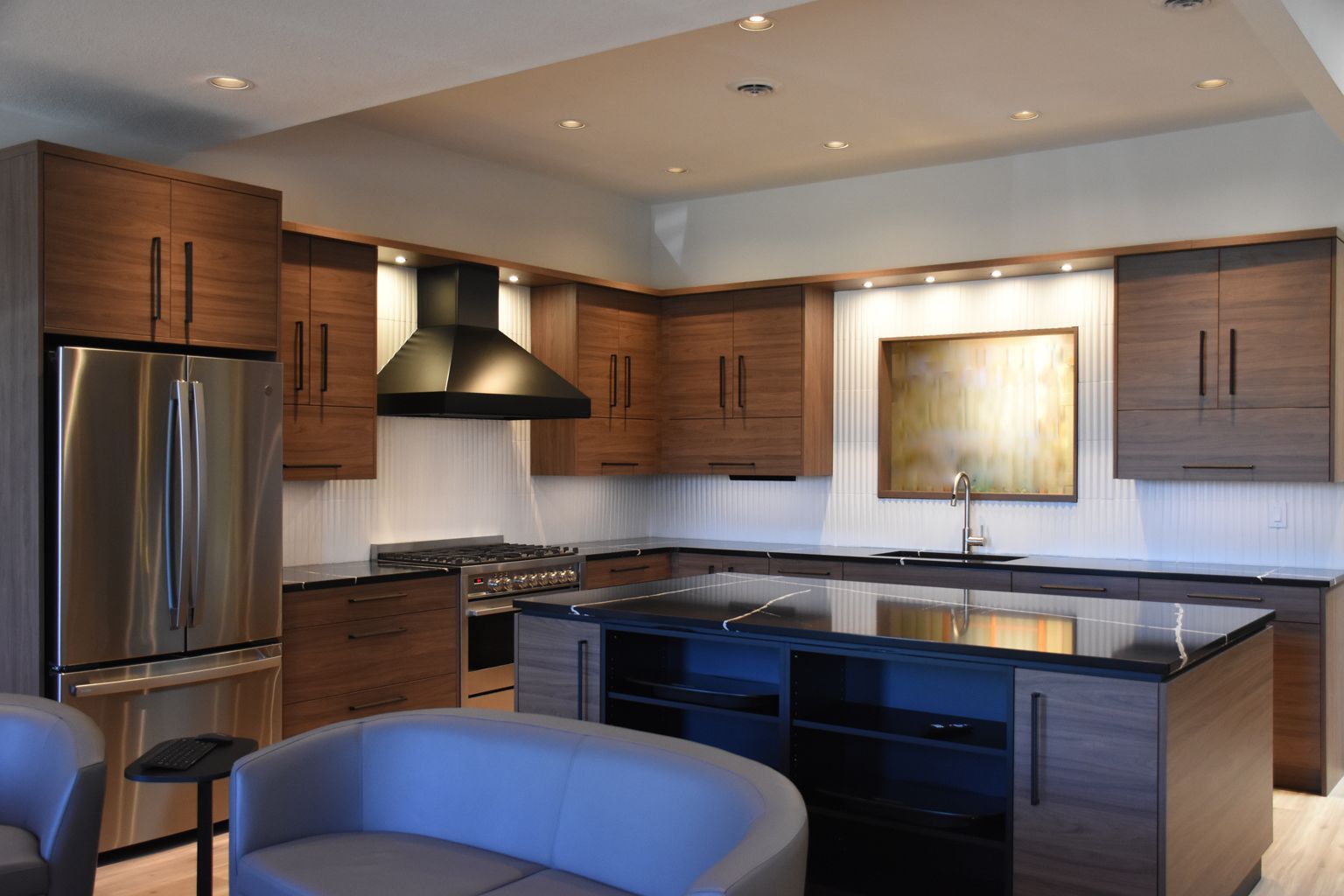 Modern kitchen with wood cabinets, stainless steel appliances, dark island, and a blue chair by the counter