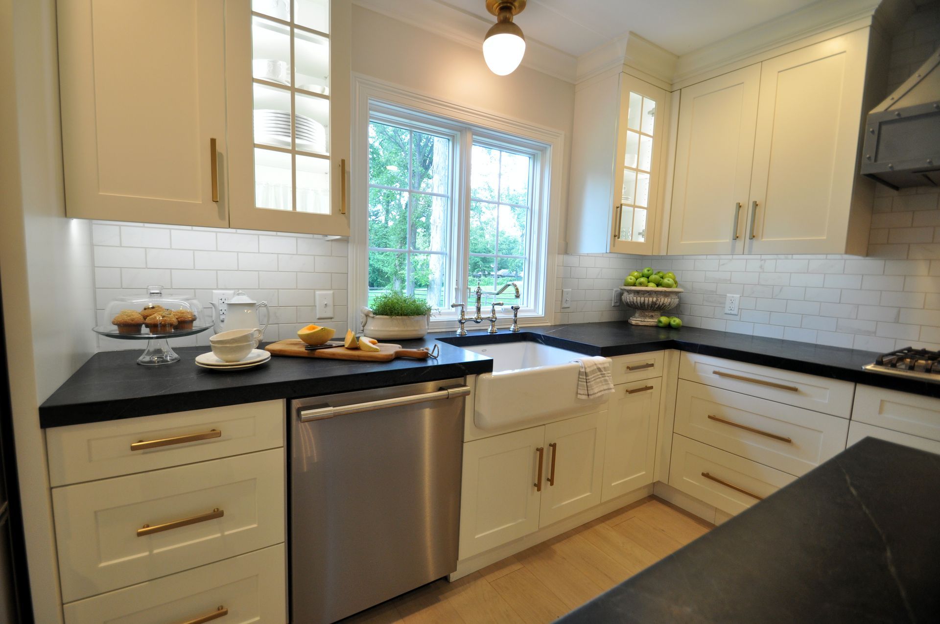 Bright white kitchen with black countertops, stainless dishwasher, and a window over the sink.