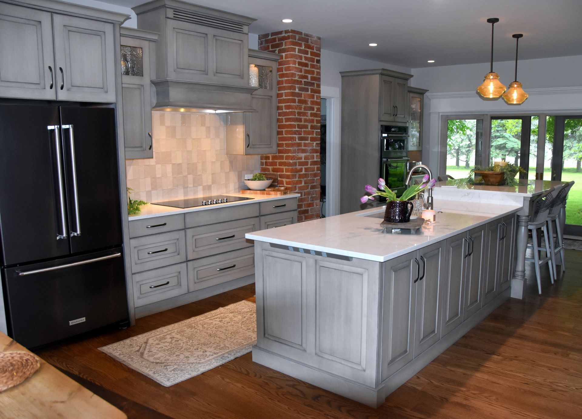 Modern kitchen with gray cabinets, black fridge, white island, pendant lights, and wood floors.