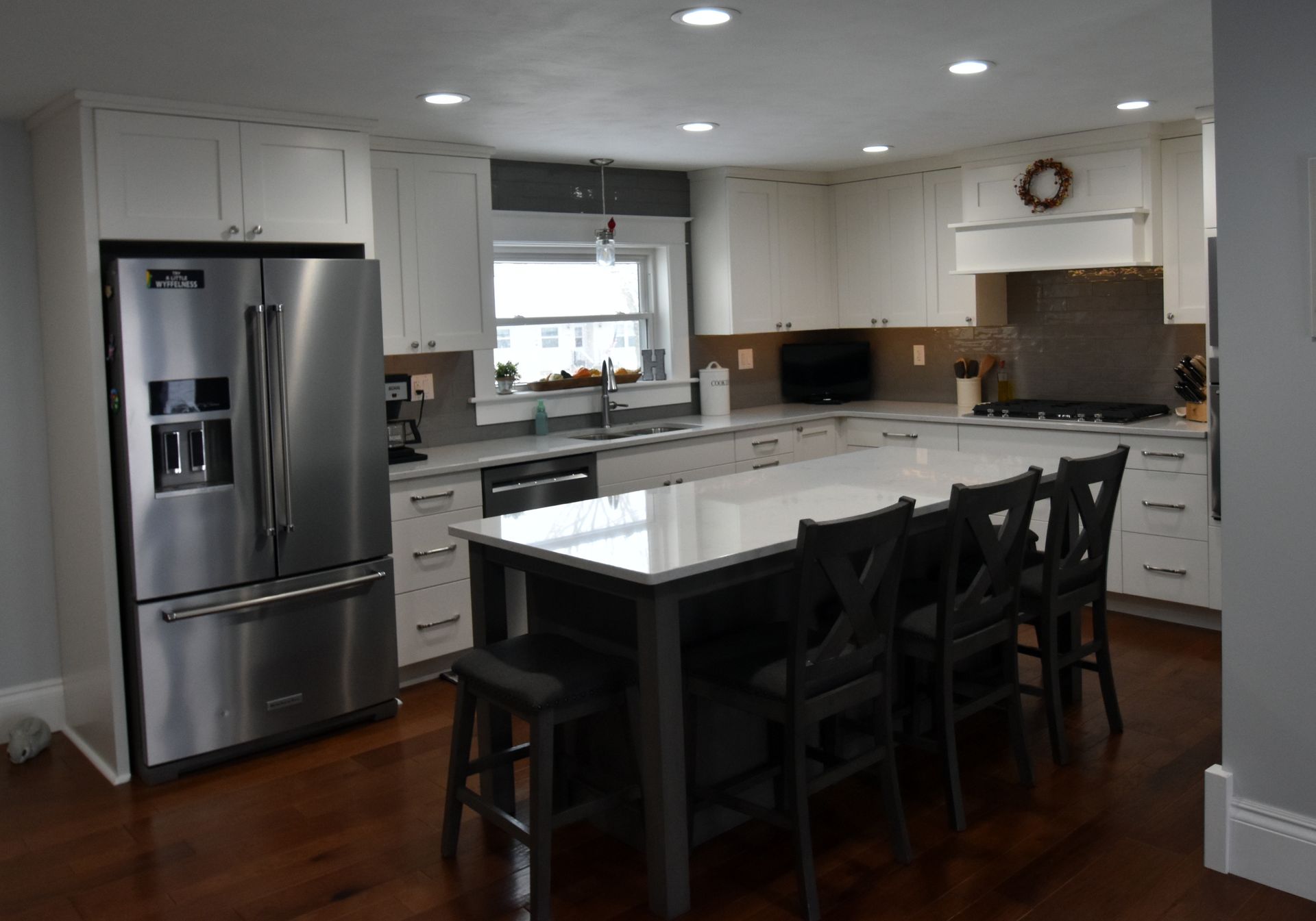 Modern white kitchen with stainless steel fridge, island, black chairs, and wood floors