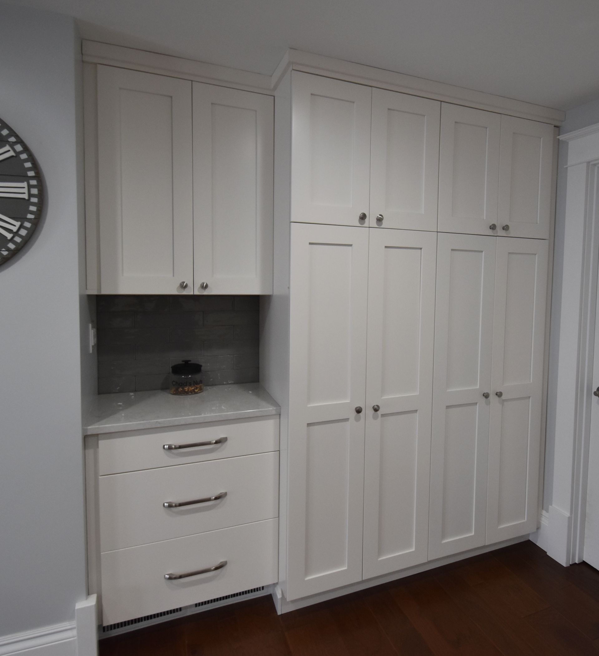 Built-in white cabinets and drawers in a hallway, with a recessed countertop nook and wall clock.