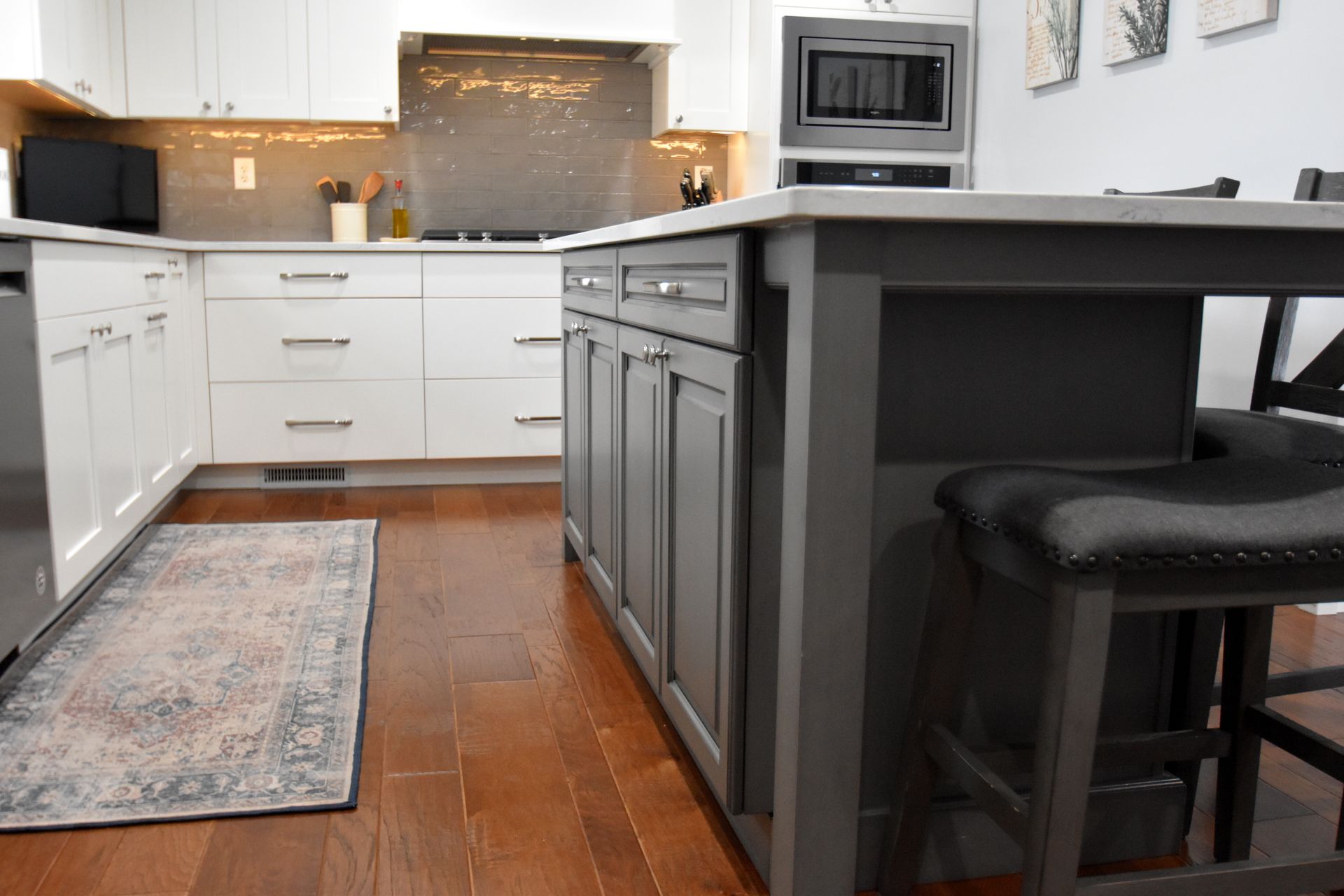 Modern kitchen with white cabinets, dark island, and hardwood floor with a small rug
