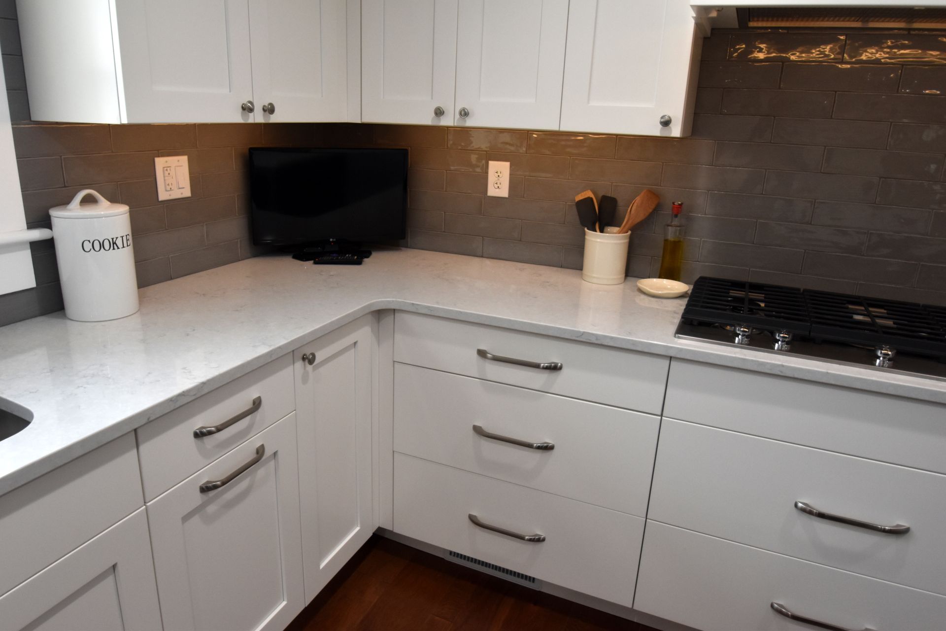 White kitchen corner with gray backsplash, white cabinets, and black cooktop on the right.