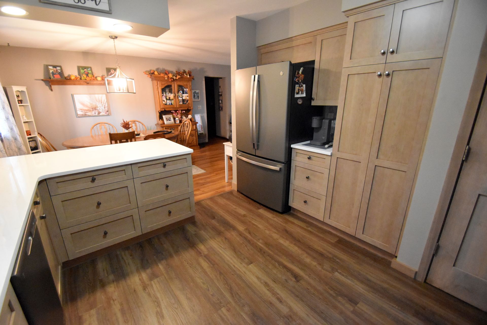 Modern kitchen with island, stainless fridge, wood floors, and light wood cabinets