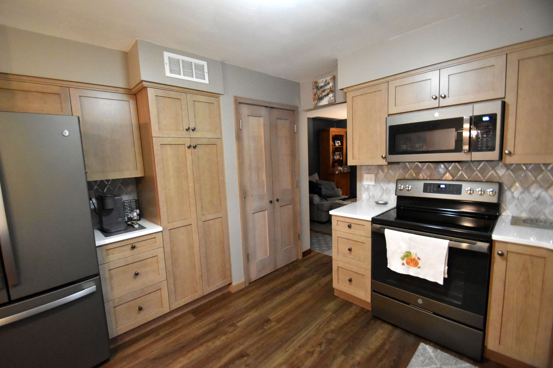 Modern kitchen with stainless steel fridge, wood cabinets, black stove, and wood-look flooring.