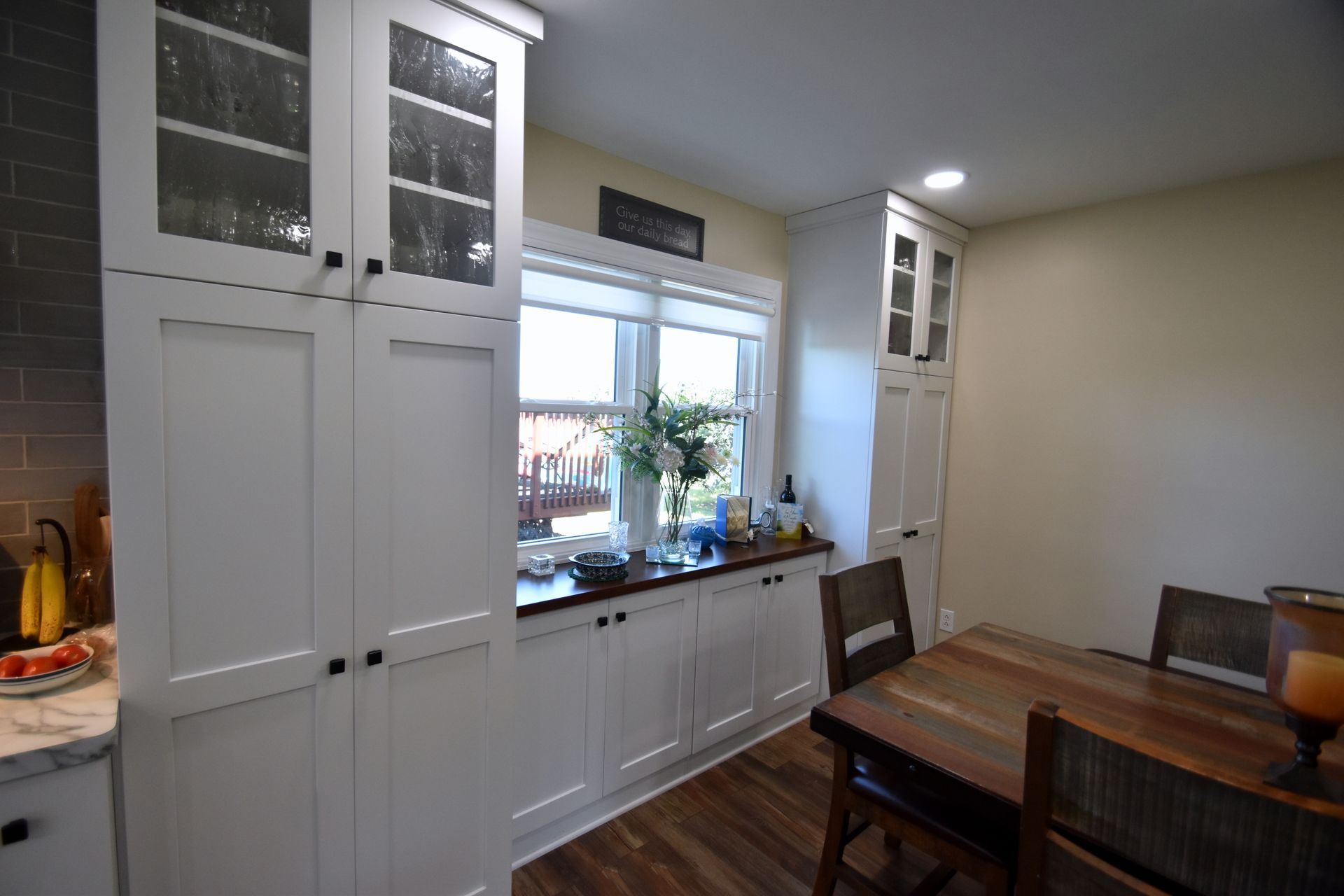 Bright kitchen-dining room with white cabinets, window, and wooden table and chairs.