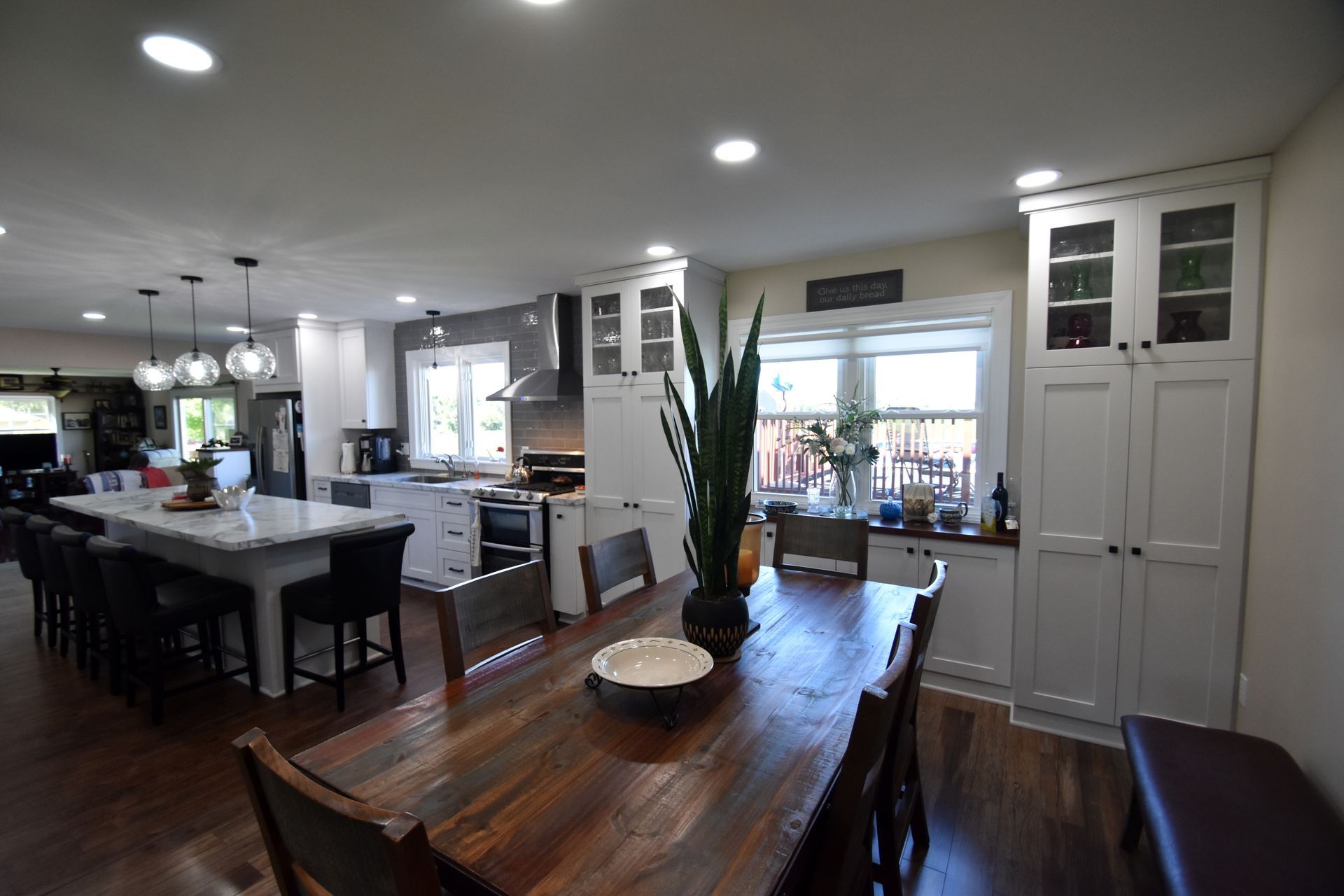 Open-plan kitchen and dining area with a wooden table, island, pendant lights, and large windows