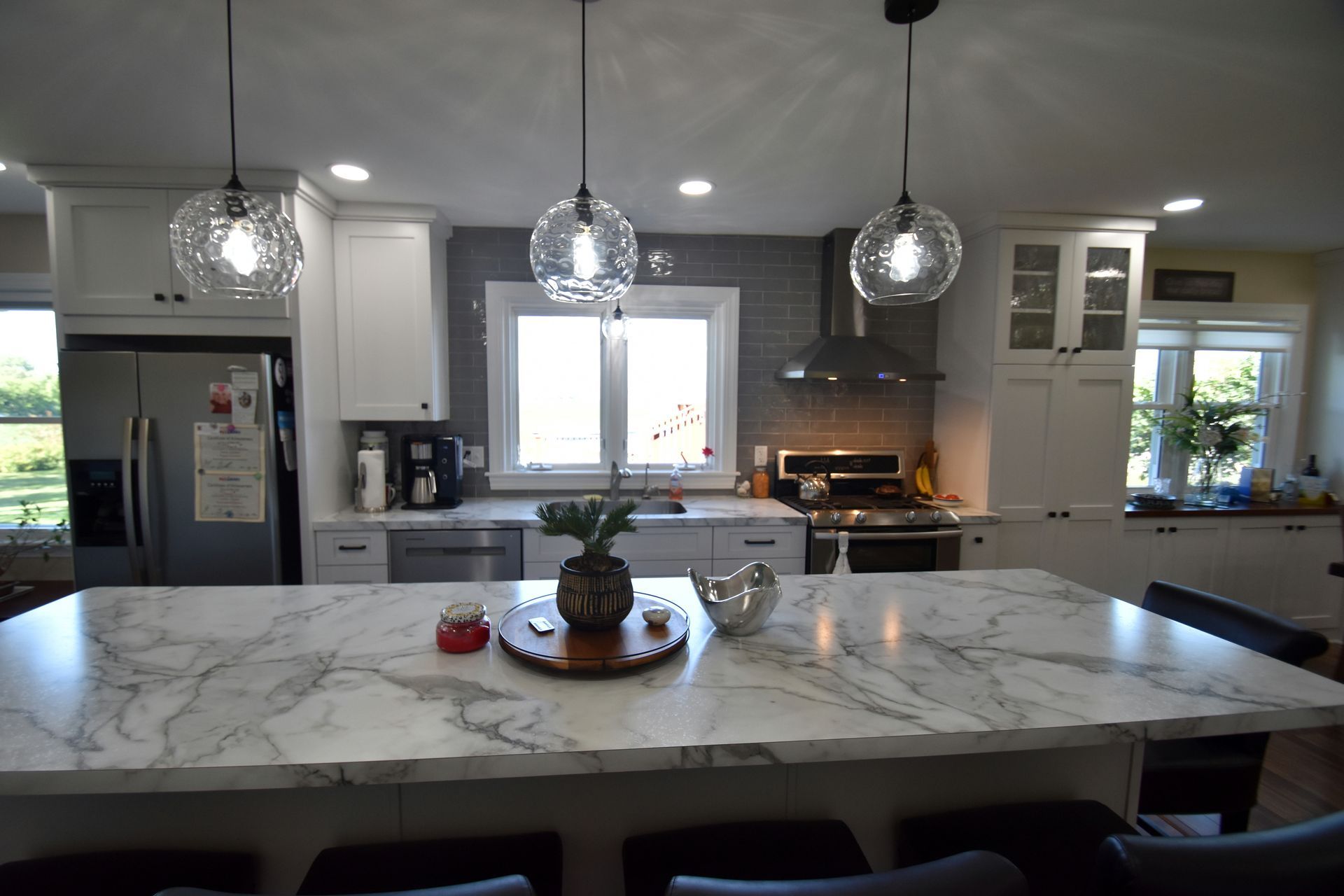 Modern kitchen with marble island, pendant lights, stainless appliances, and a window above the sink