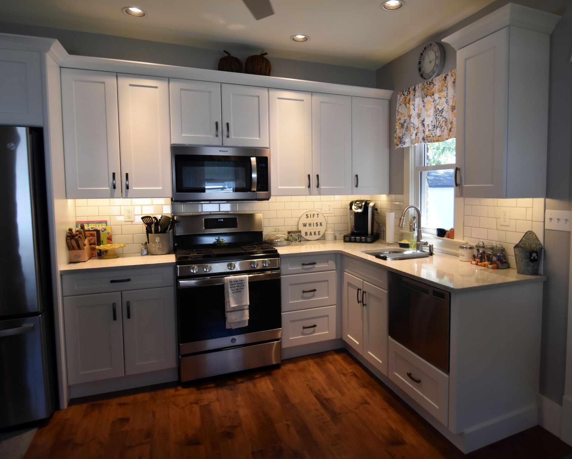 Modern kitchen with white cabinets, stainless steel appliances, and warm wood floors