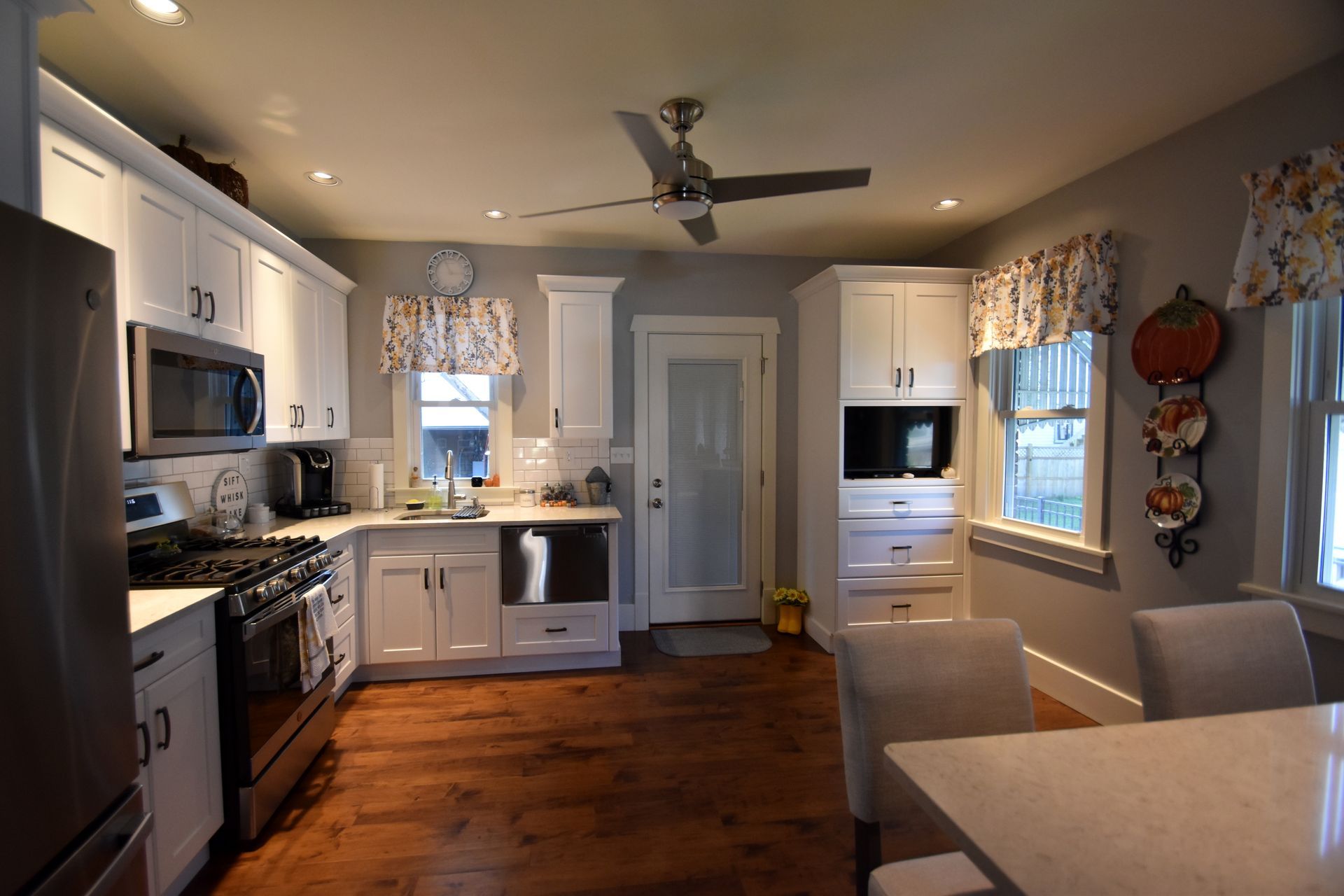 Bright modern kitchen with white cabinets, stainless appliances, wood floor, and a dining table by the window