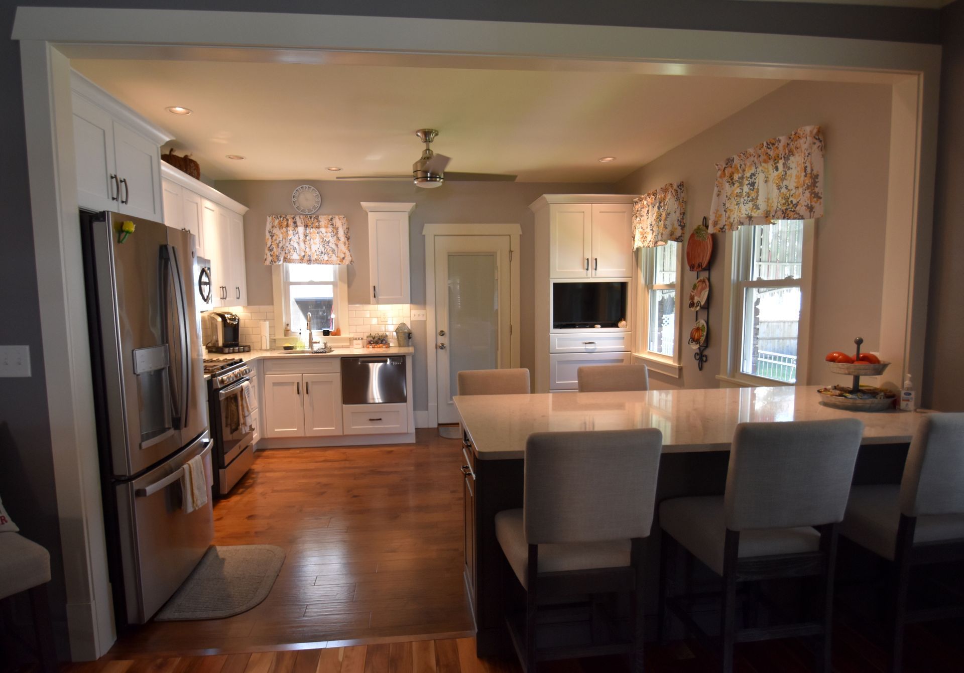 Open kitchen with white cabinets, dark wood floors, large island, and stainless steel refrigerator.