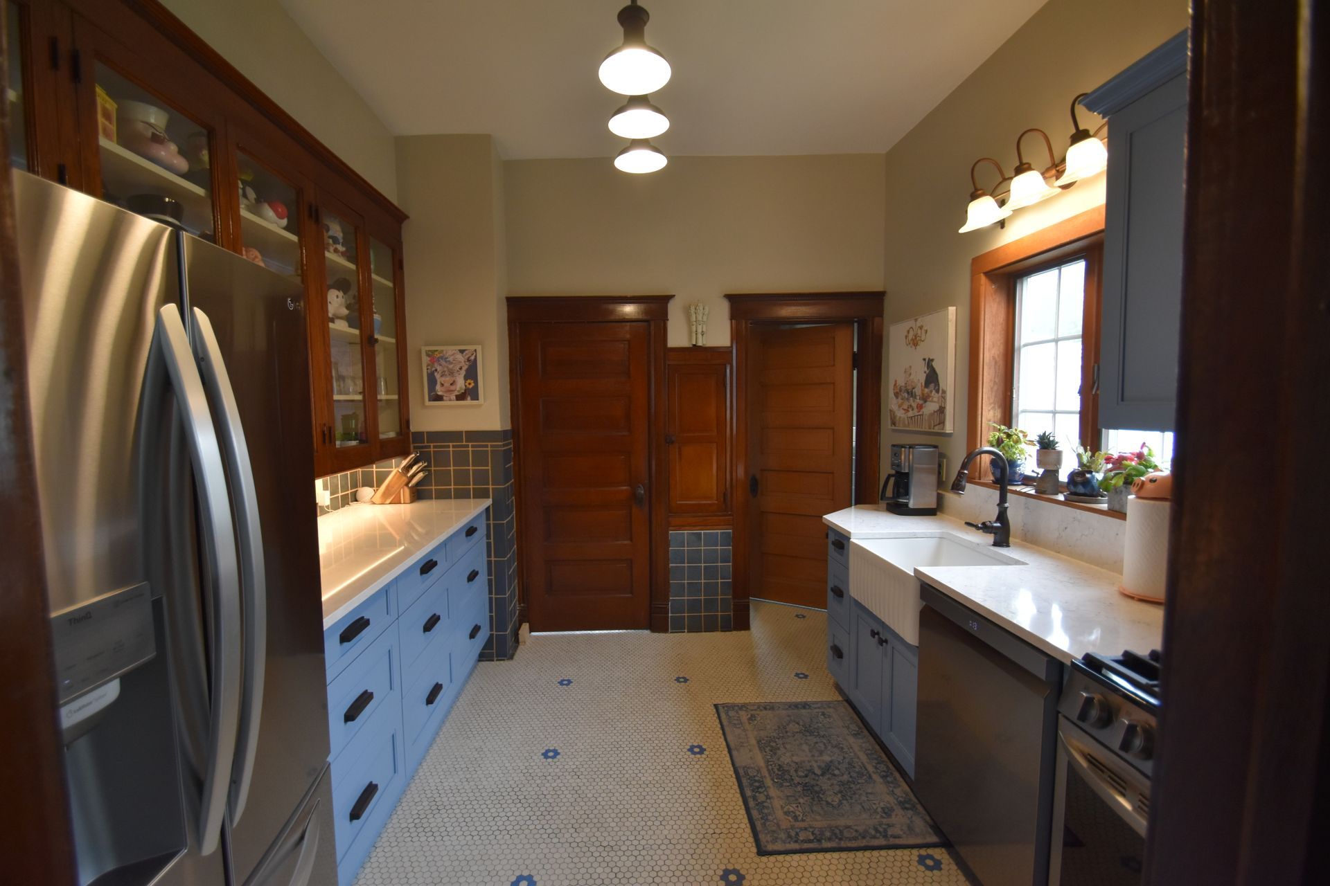 Narrow kitchen with stainless steel fridge, blue cabinets, wood doors, and a window over the sink.
