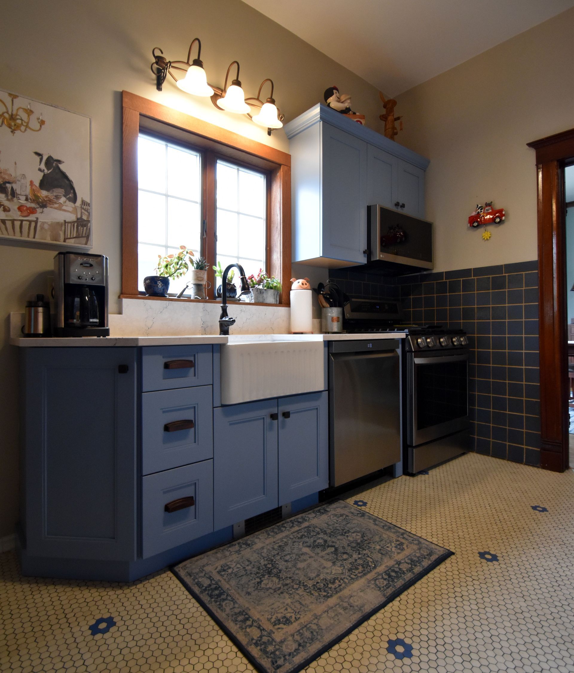 Blue kitchen cabinets with stainless dishwasher, window, stove, and patterned tile floor under warm lights