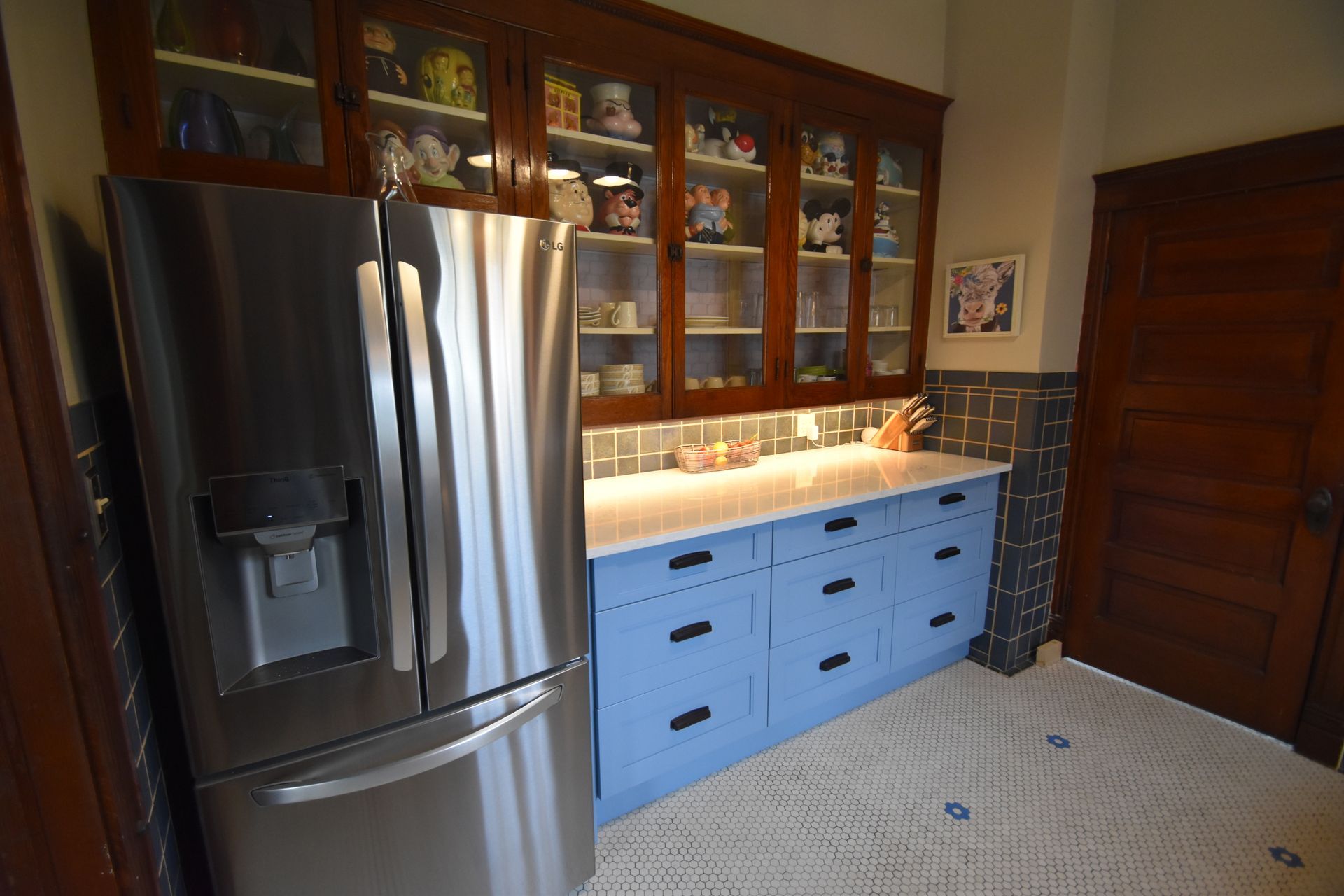 Kitchen with stainless steel fridge, blue cabinets, glass-front upper cabinets, and tile floor.