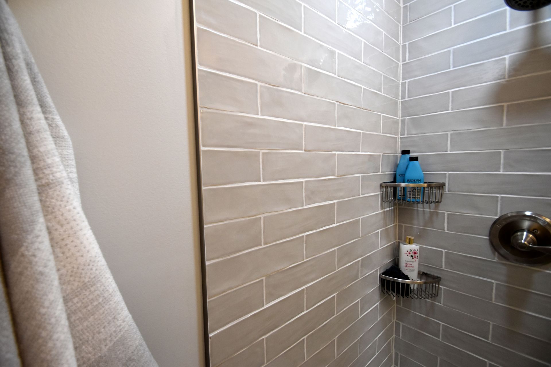 Tiled shower corner with soap caddy, bottles, and a showerhead