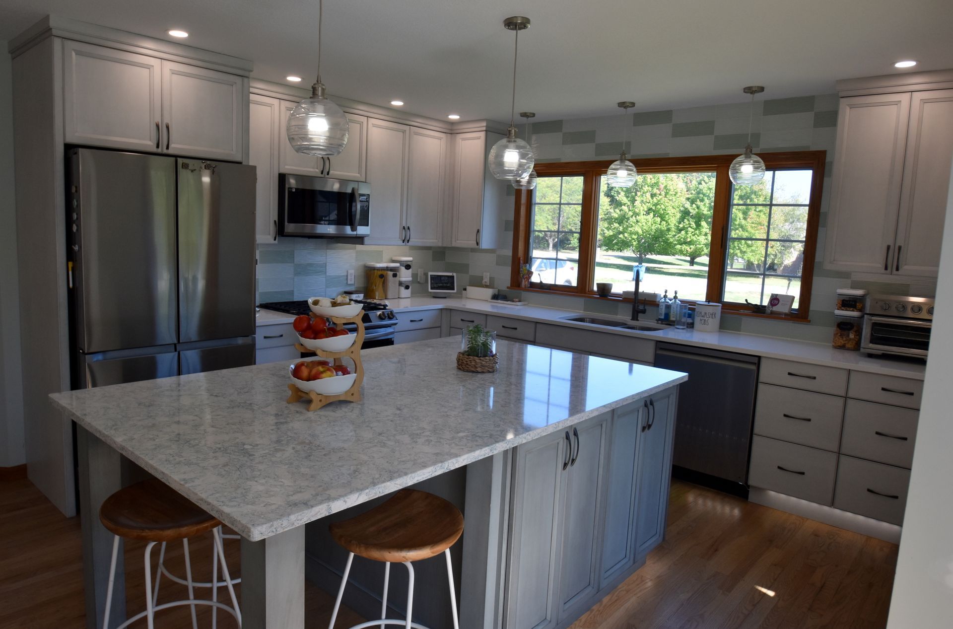 Modern kitchen with gray cabinets, large island, stainless appliances, and a view of trees through the window