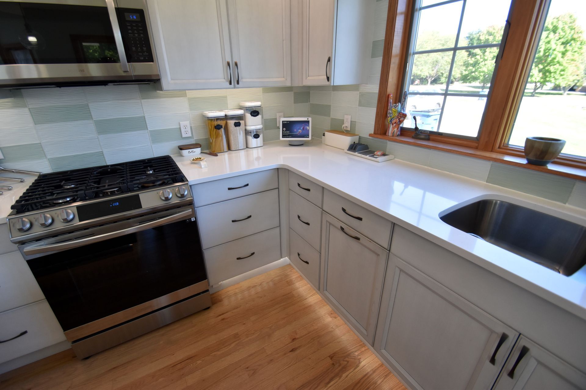 Modern kitchen with white cabinets, black stove, wood floor, and a window over the sink.