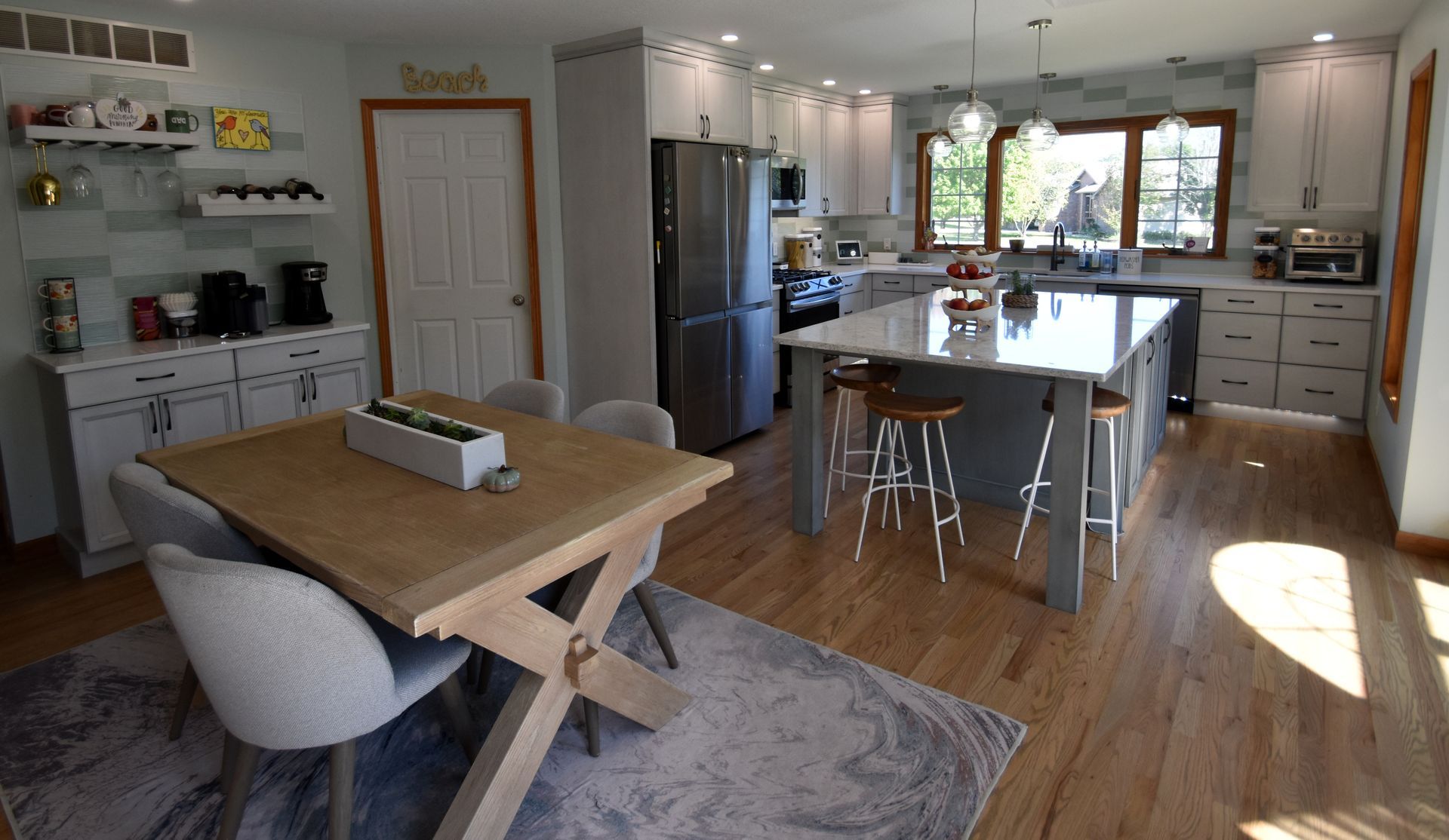 Bright modern kitchen and dining area with wood floors, island, stools, and a table by the window.
