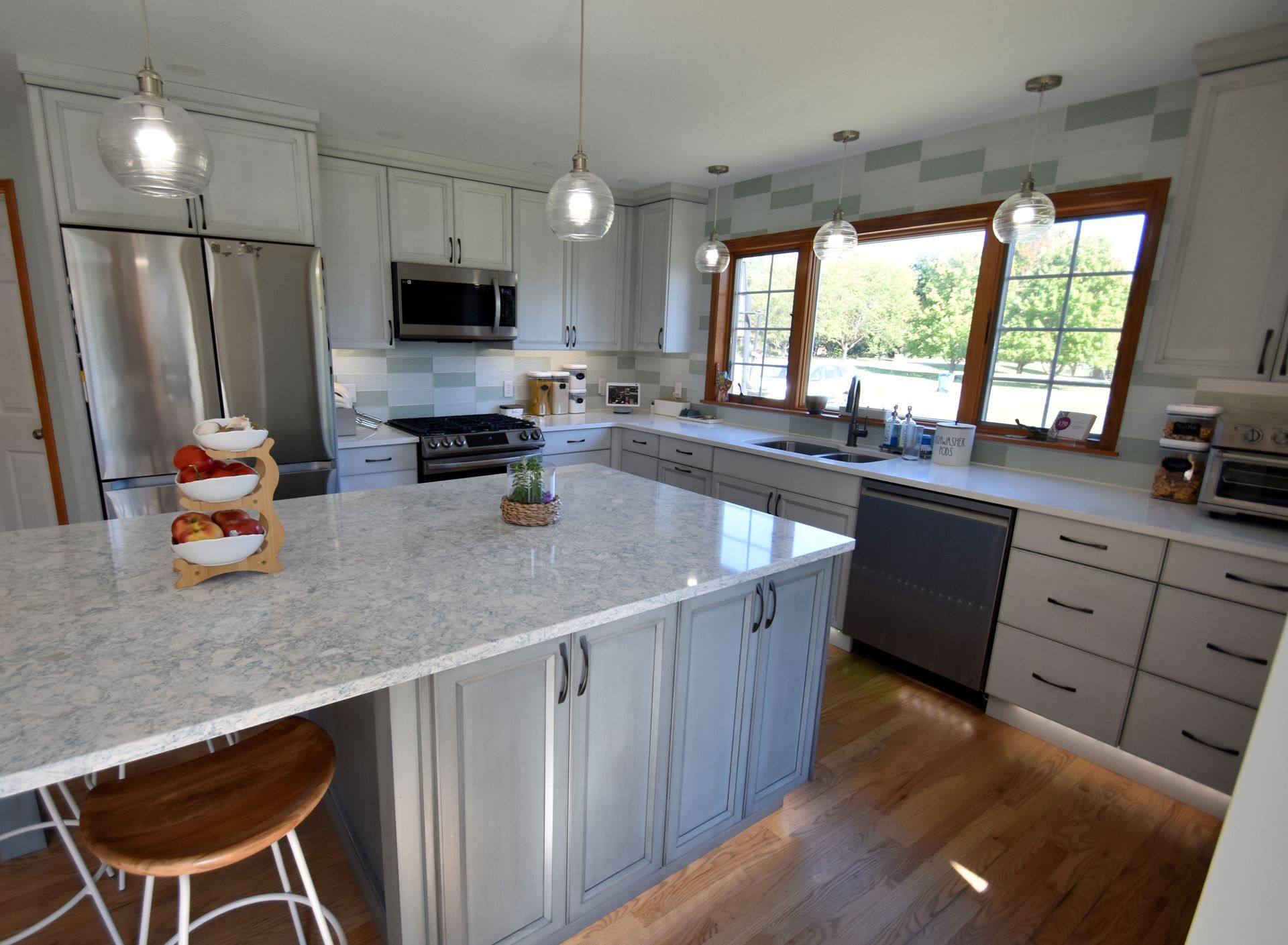 Bright modern kitchen with white island, gray cabinets, wood floor, and large window above the sink