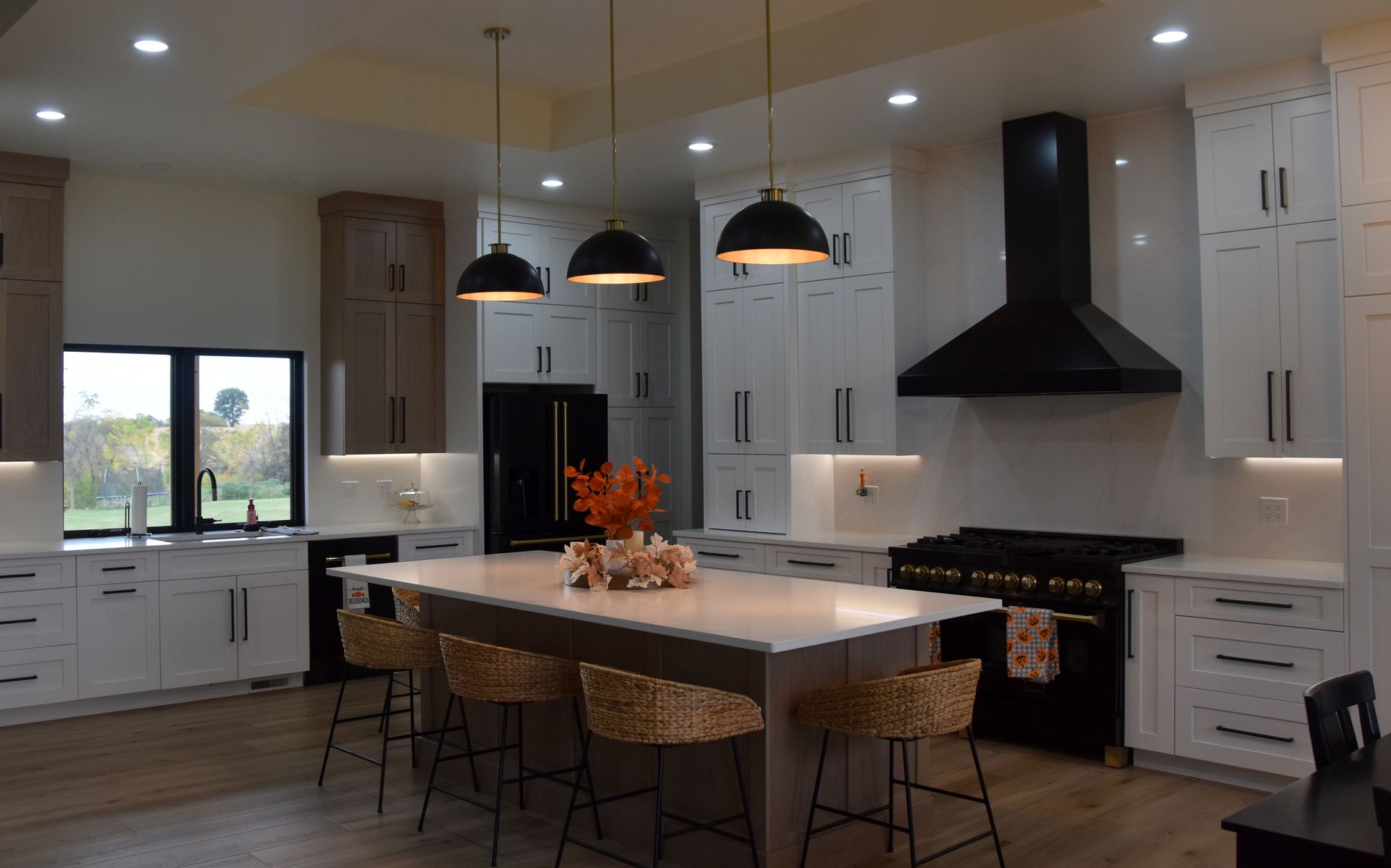Modern kitchen with white cabinets, large island, pendant lights, black range hood, and wood flooring.