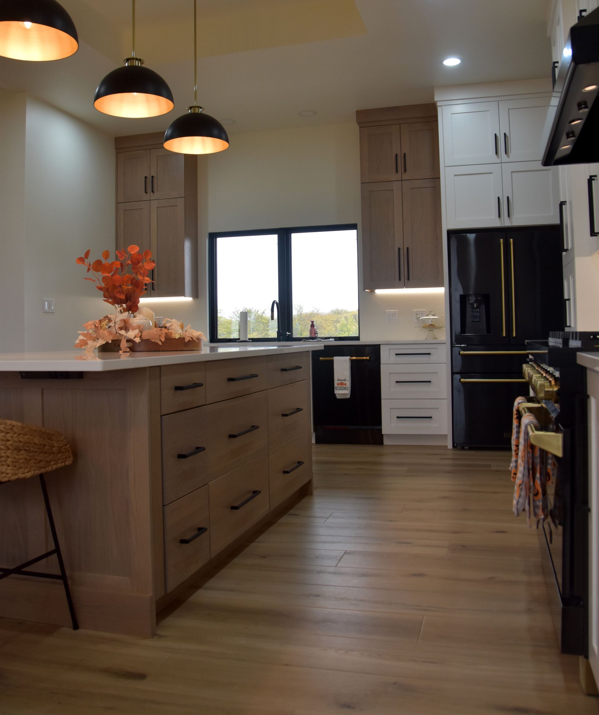 Modern kitchen with a large island, pendant lights, black appliances, and a window view.