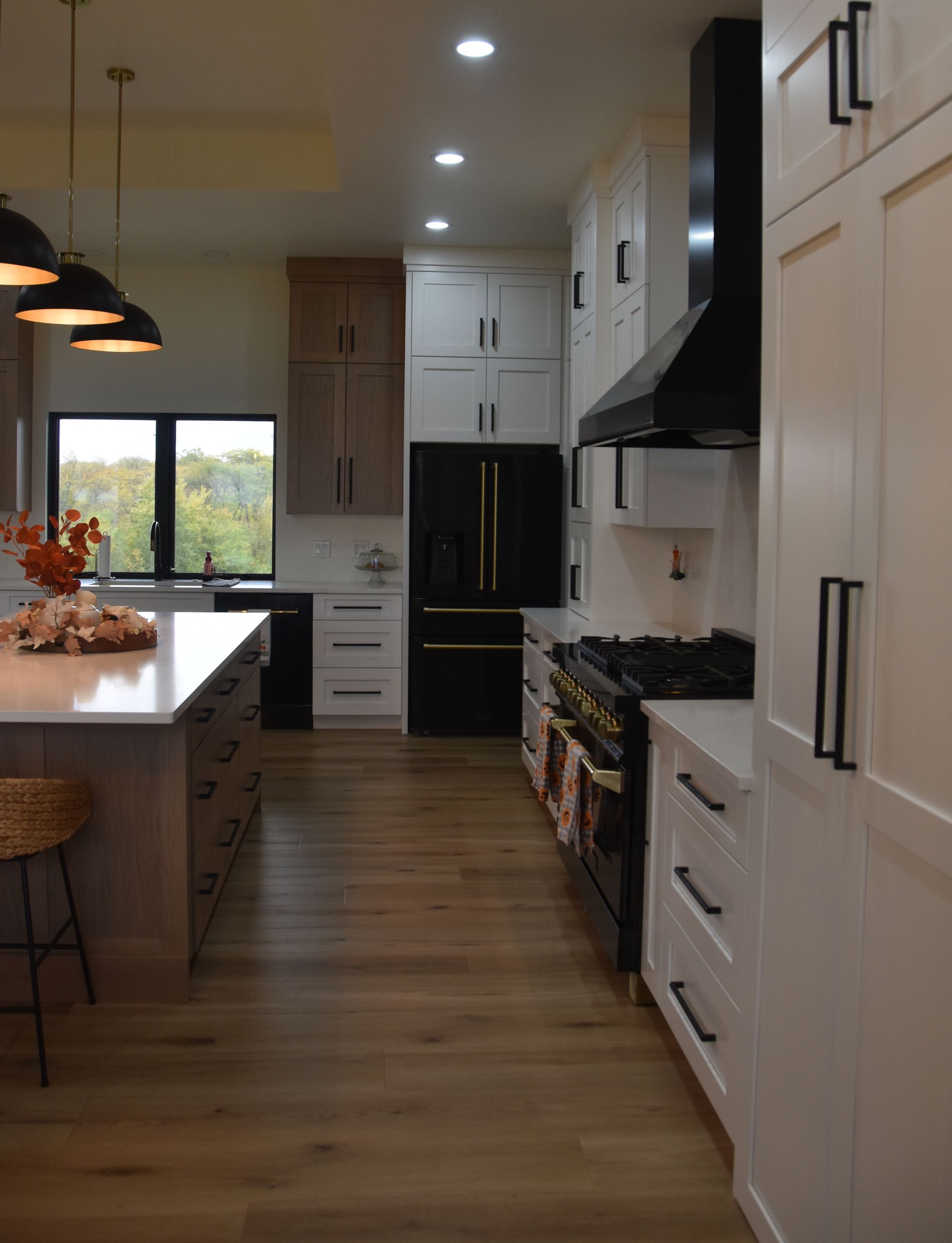 Modern kitchen with white cabinets, black appliances, wood floors, and a large island by a window.