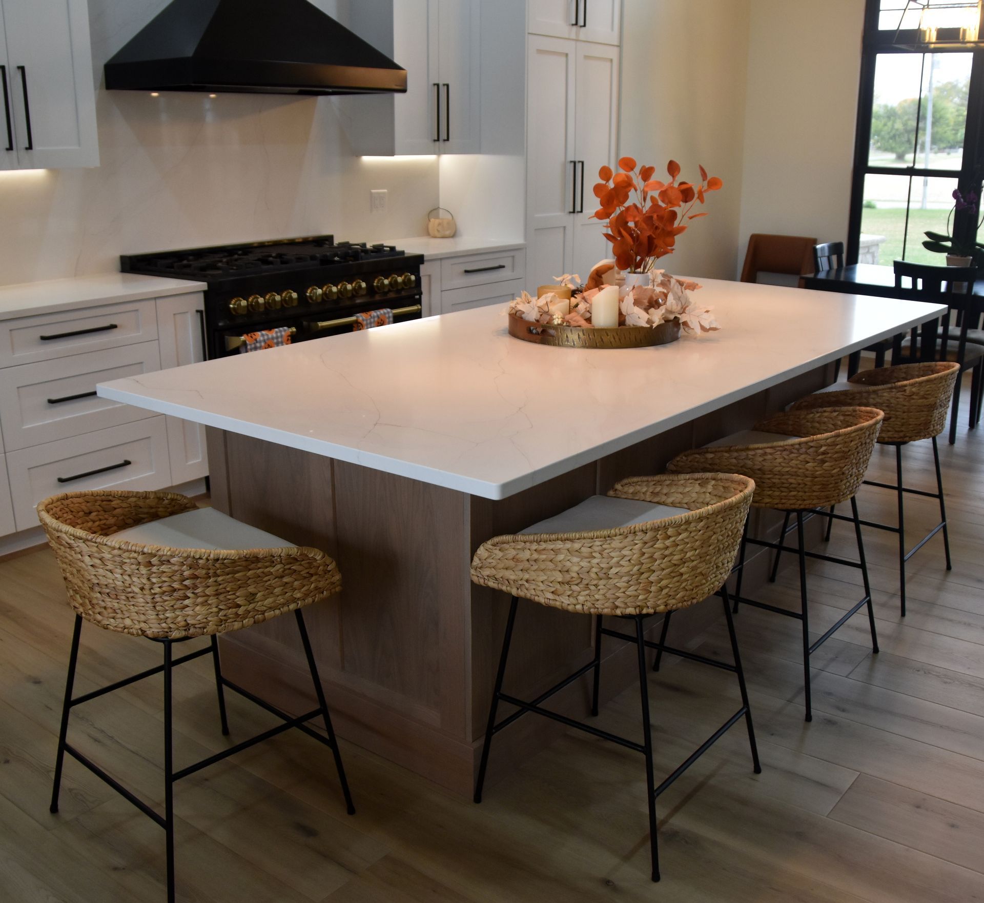 Modern kitchen with a large white island, woven stools, and a black range hood.