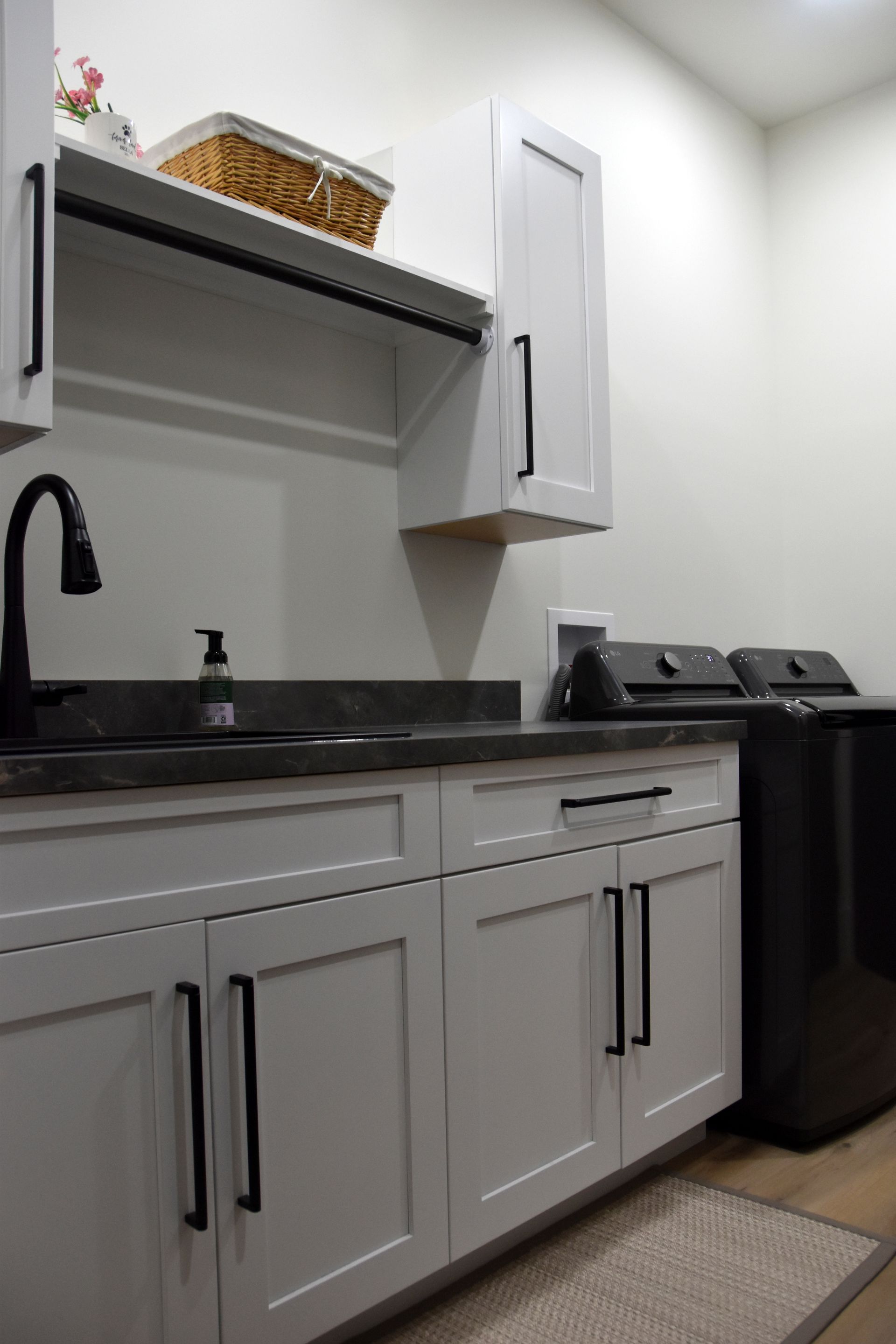 Modern laundry room with white cabinets, black countertop, sink, and stacked washer-dryer.