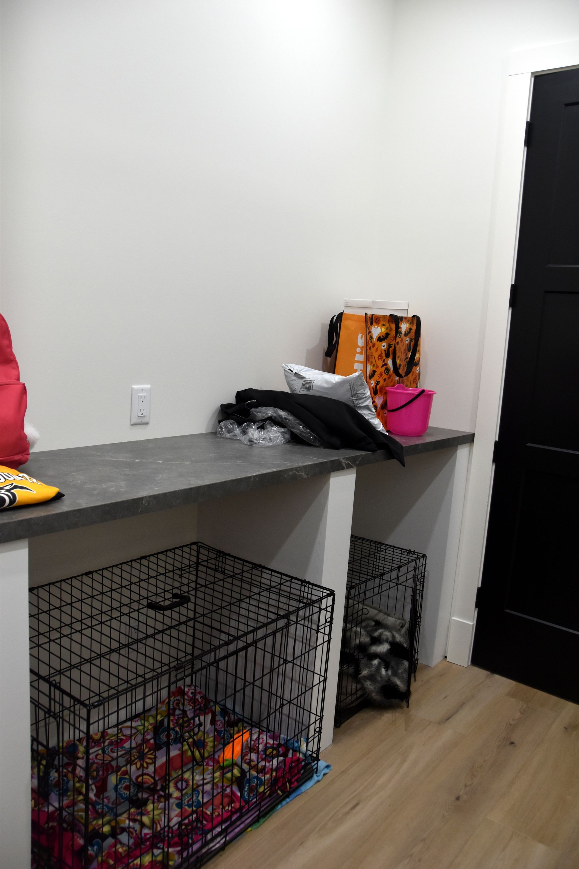 Small room with a white wall, gray shelf, pet crate, black cabinet, and bags on top of the shelf.
