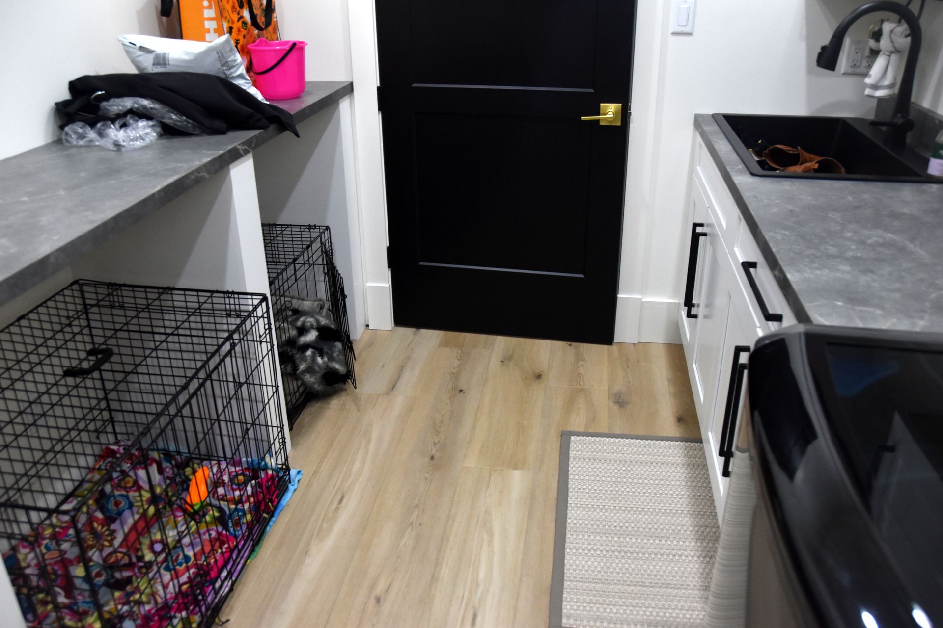 Modern laundry room with black door, gray counters, wire basket, and washing machine.