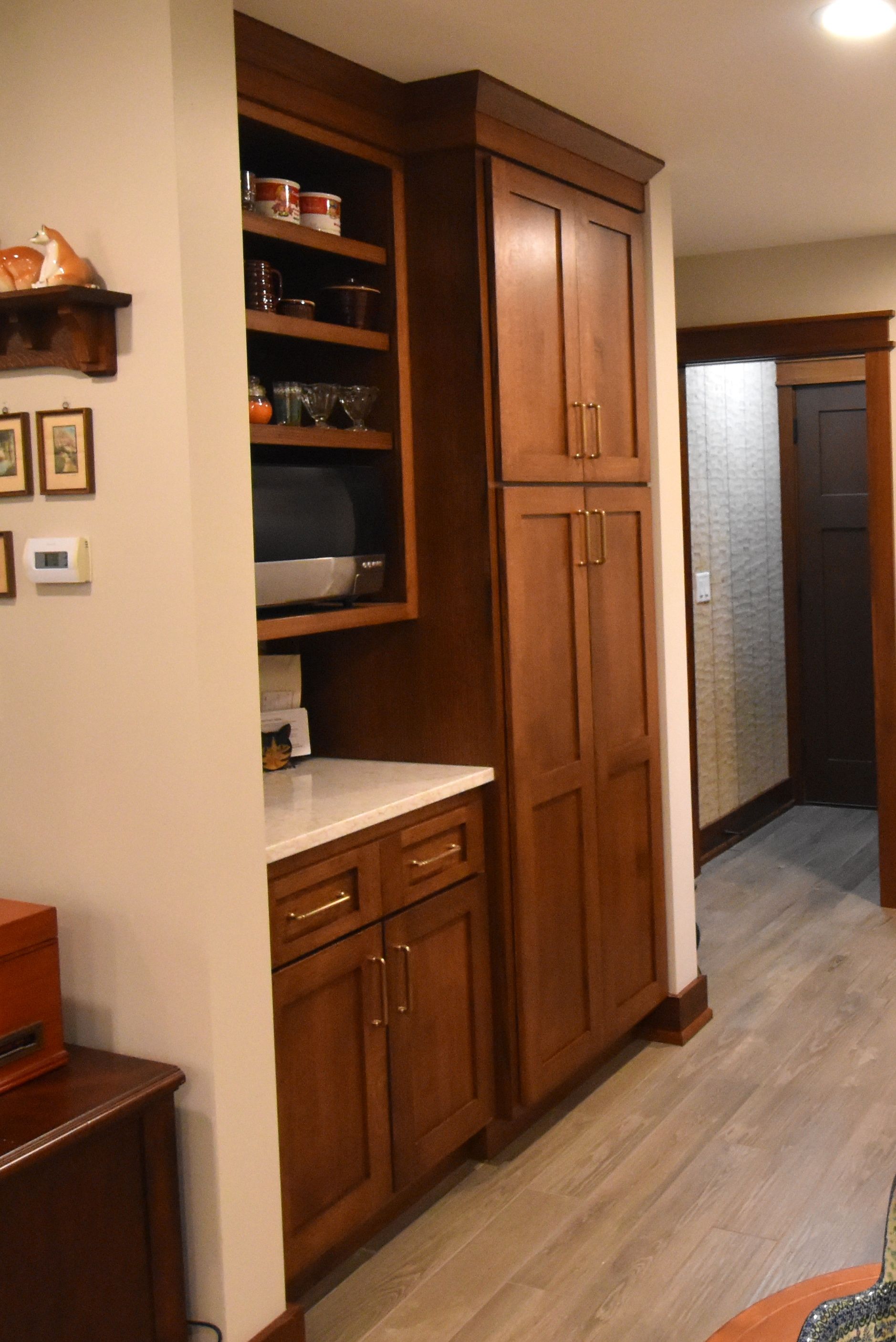 Narrow hallway with wooden cabinets, built-in shelves, and a doorway leading to a tiled bathroom.