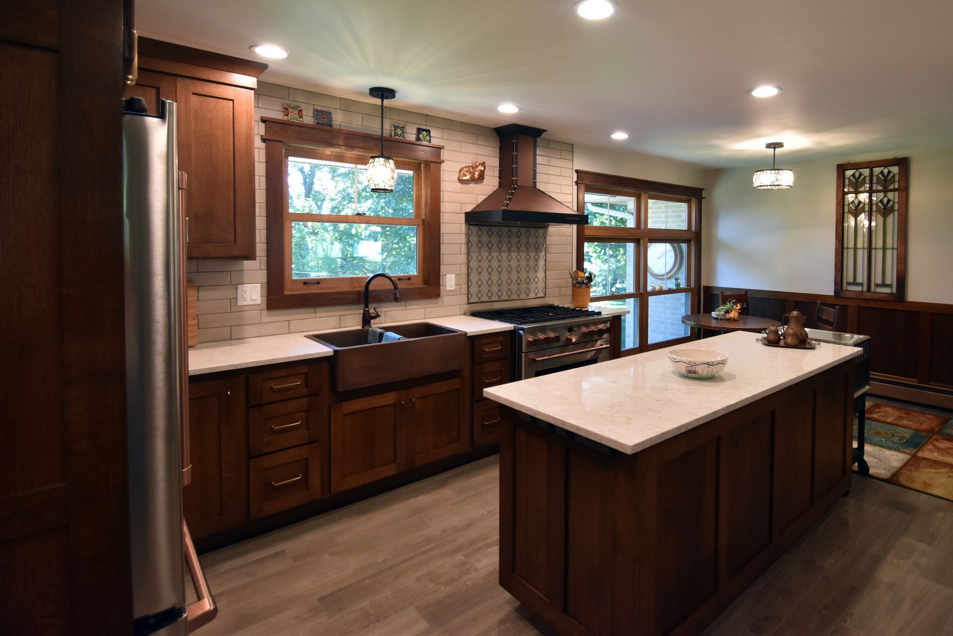 Modern kitchen with dark wood cabinets, large island, and tiled backsplash, warmly lit by windows and ceiling lights