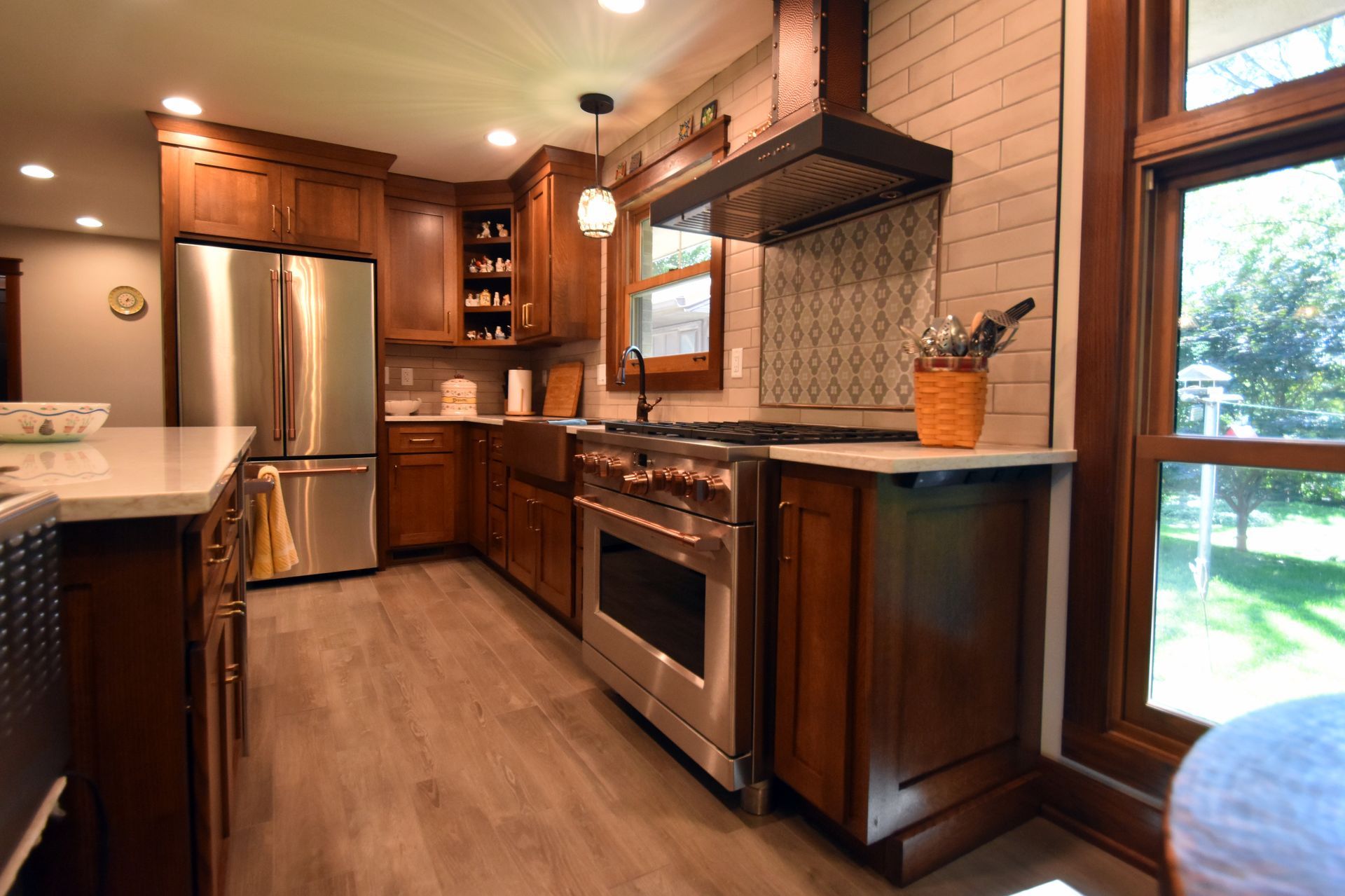 Warm kitchen with stainless steel appliances, wood cabinets, and a view of a green backyard.