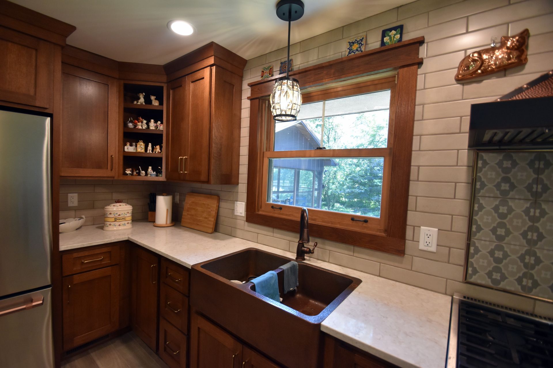 Cozy kitchen with wood cabinets, white countertops, stainless fridge, and sink under a window.