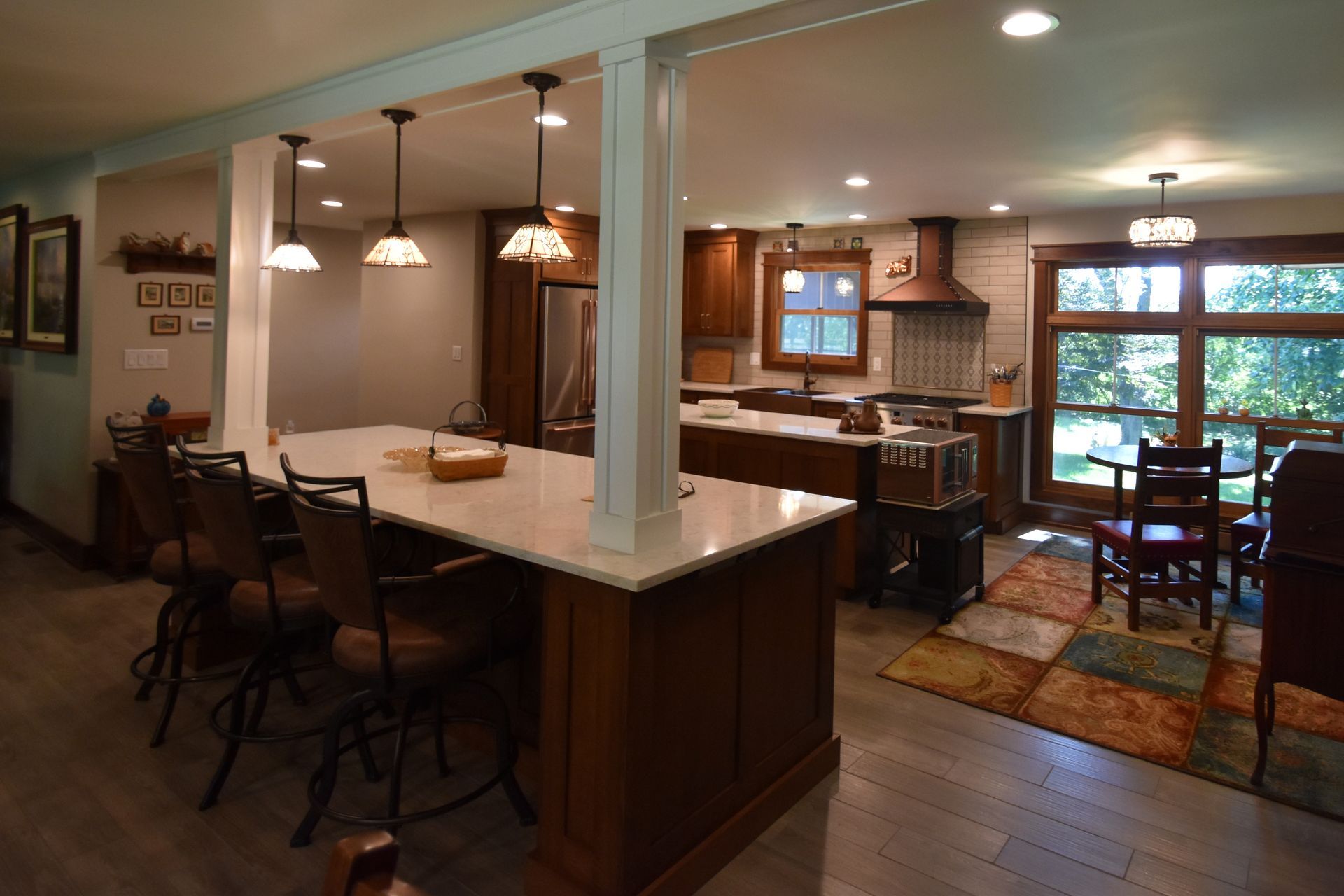 Open kitchen and dining area with white island, pendant lights, wood floors, and windowed breakfast nook.