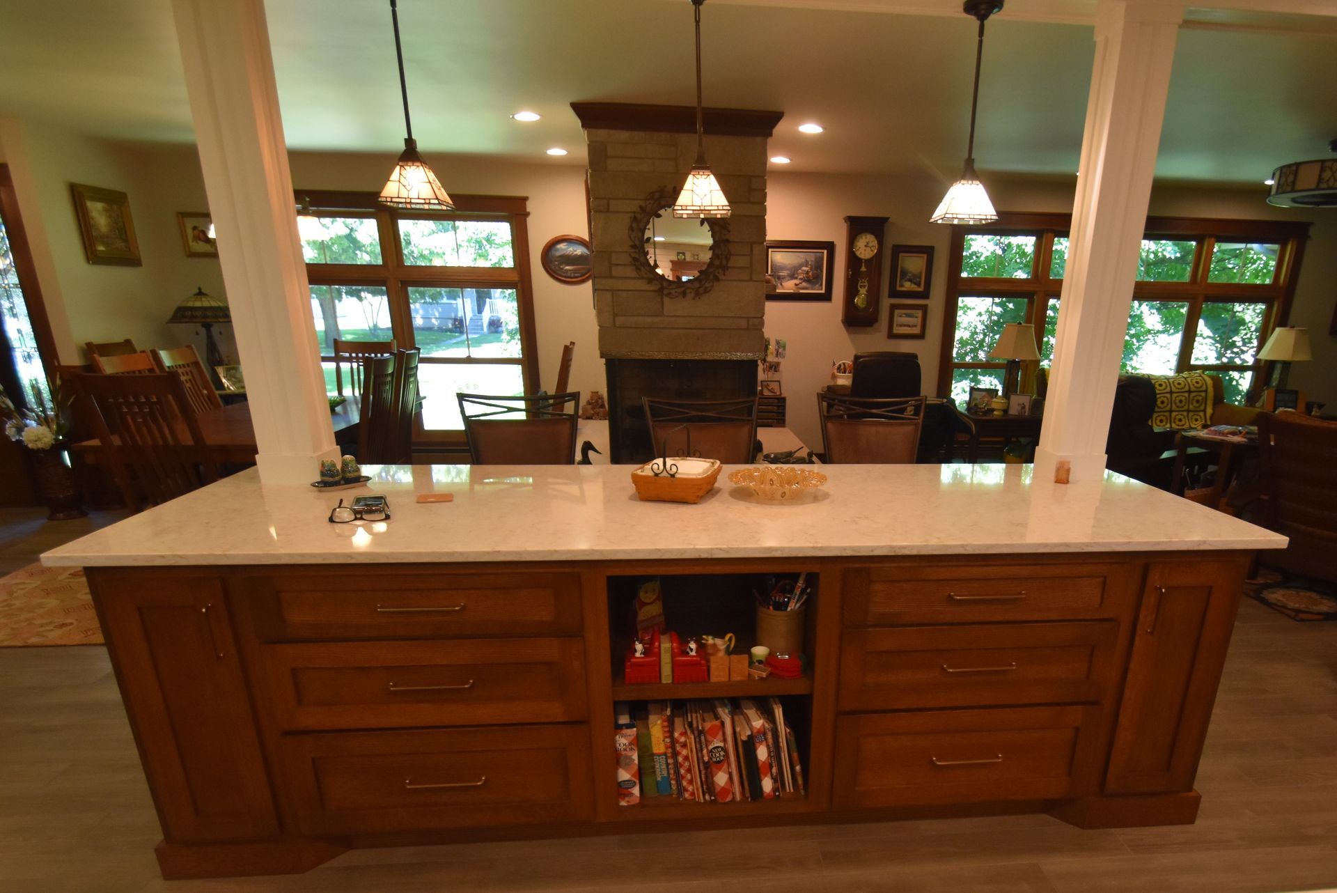 Kitchen island with white countertop and wooden cabinets, open shelf of snacks, overlooking a cozy living room