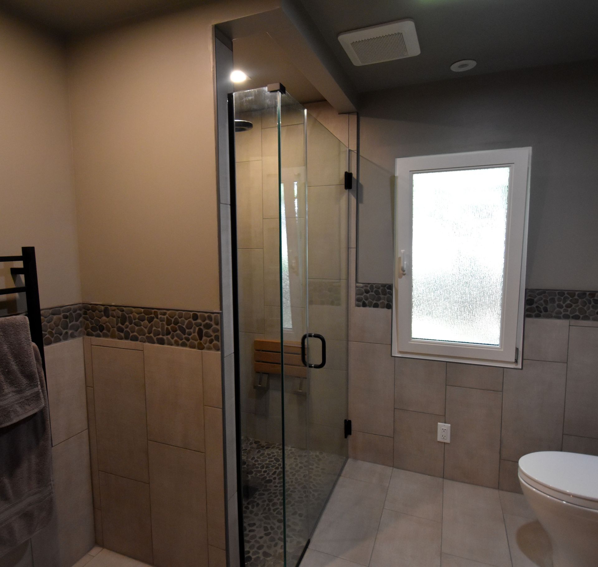 Modern tiled bathroom with glass shower, frosted window, and toilet.