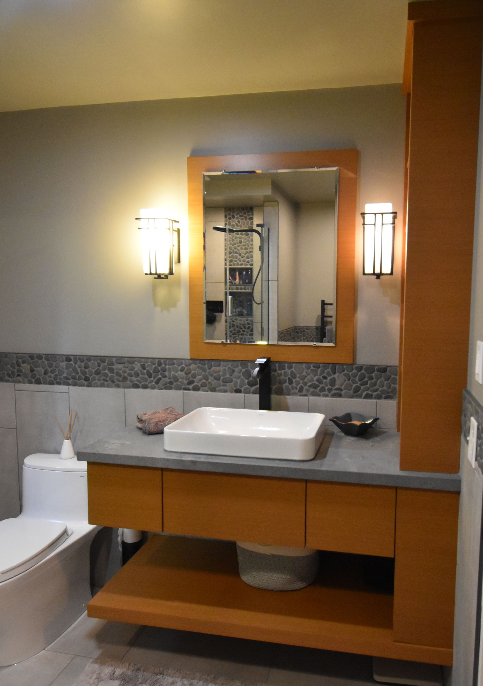 Modern bathroom vanity with sink, mirror, wall sconces, and wood cabinets.