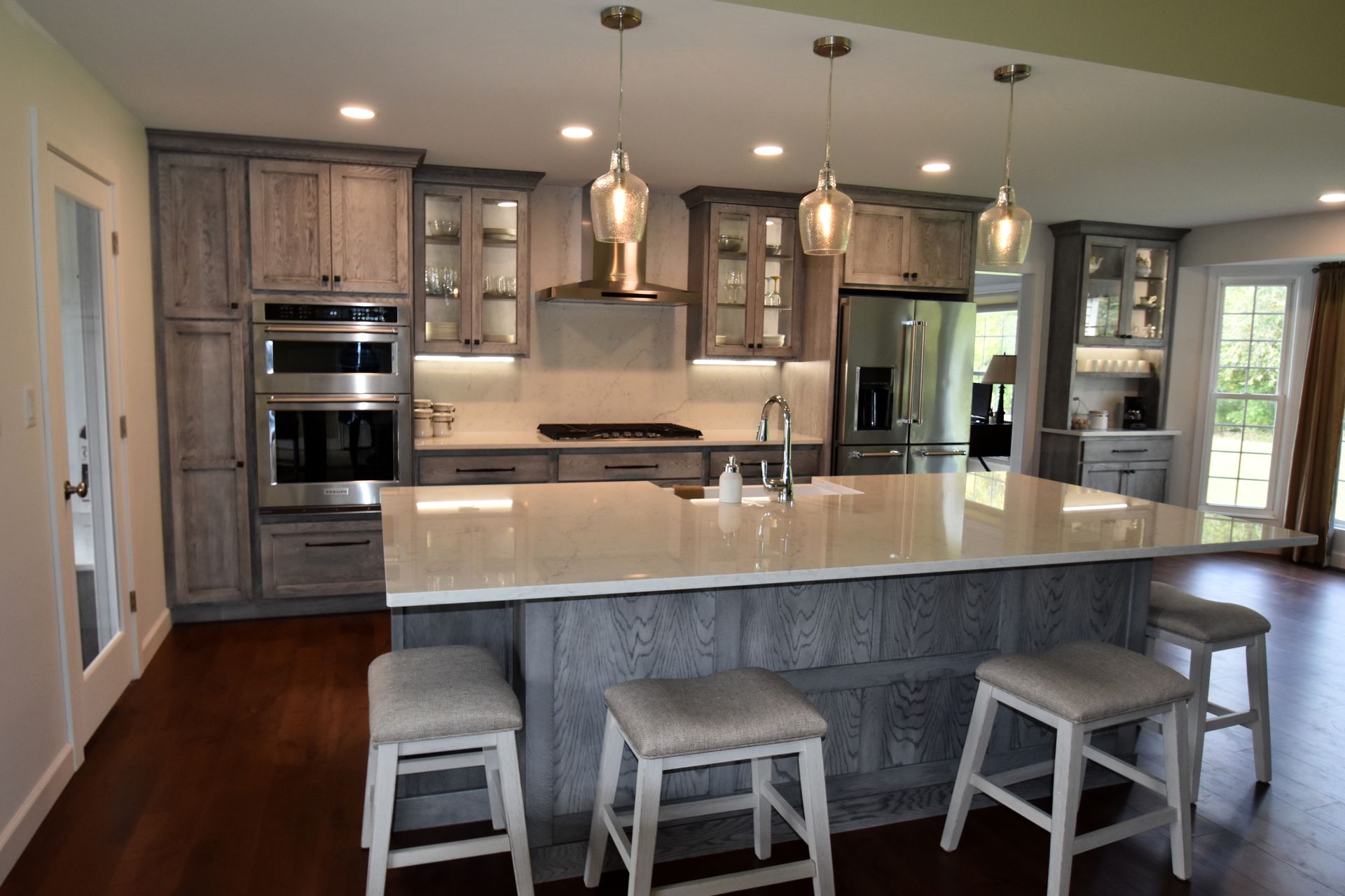 Modern kitchen with gray cabinets, white island, pendant lights, and four stools