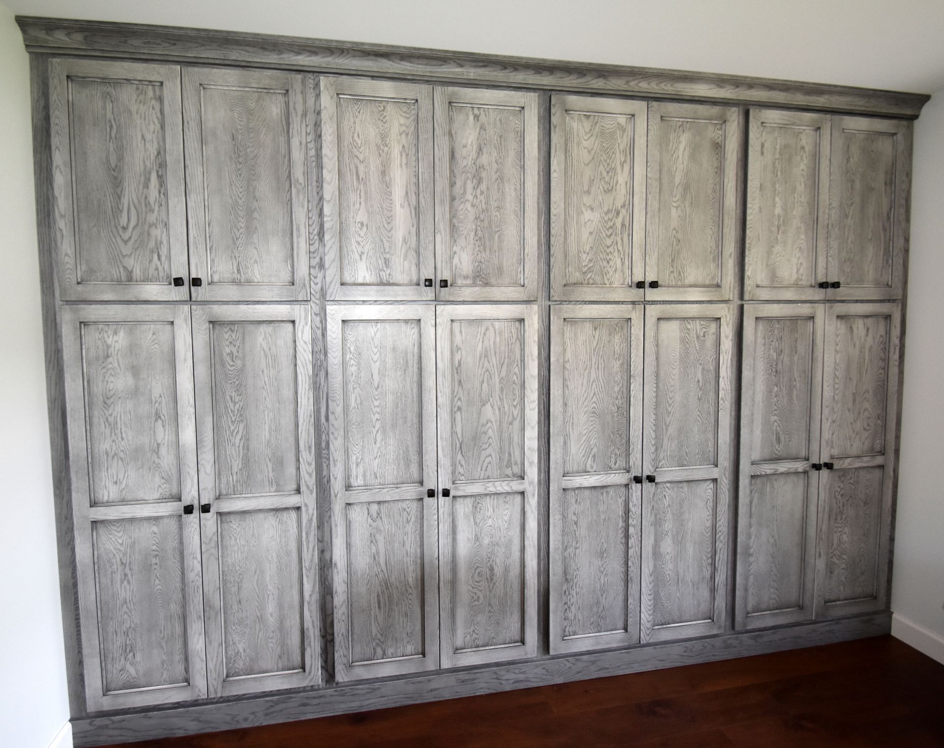 Large white built-in cabinet wall with multiple paneled doors in a room, above a dark wood floor