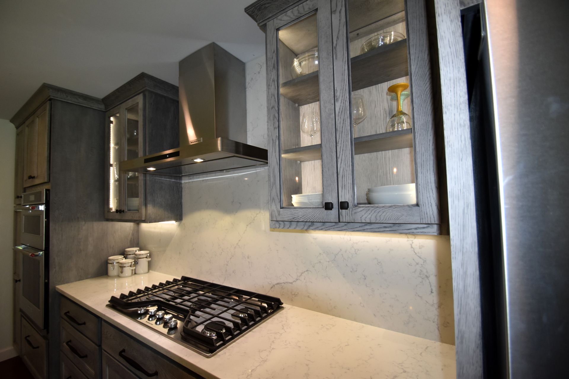 Modern kitchen with gray cabinets, marble backsplash, gas stove, and stainless steel range hood.