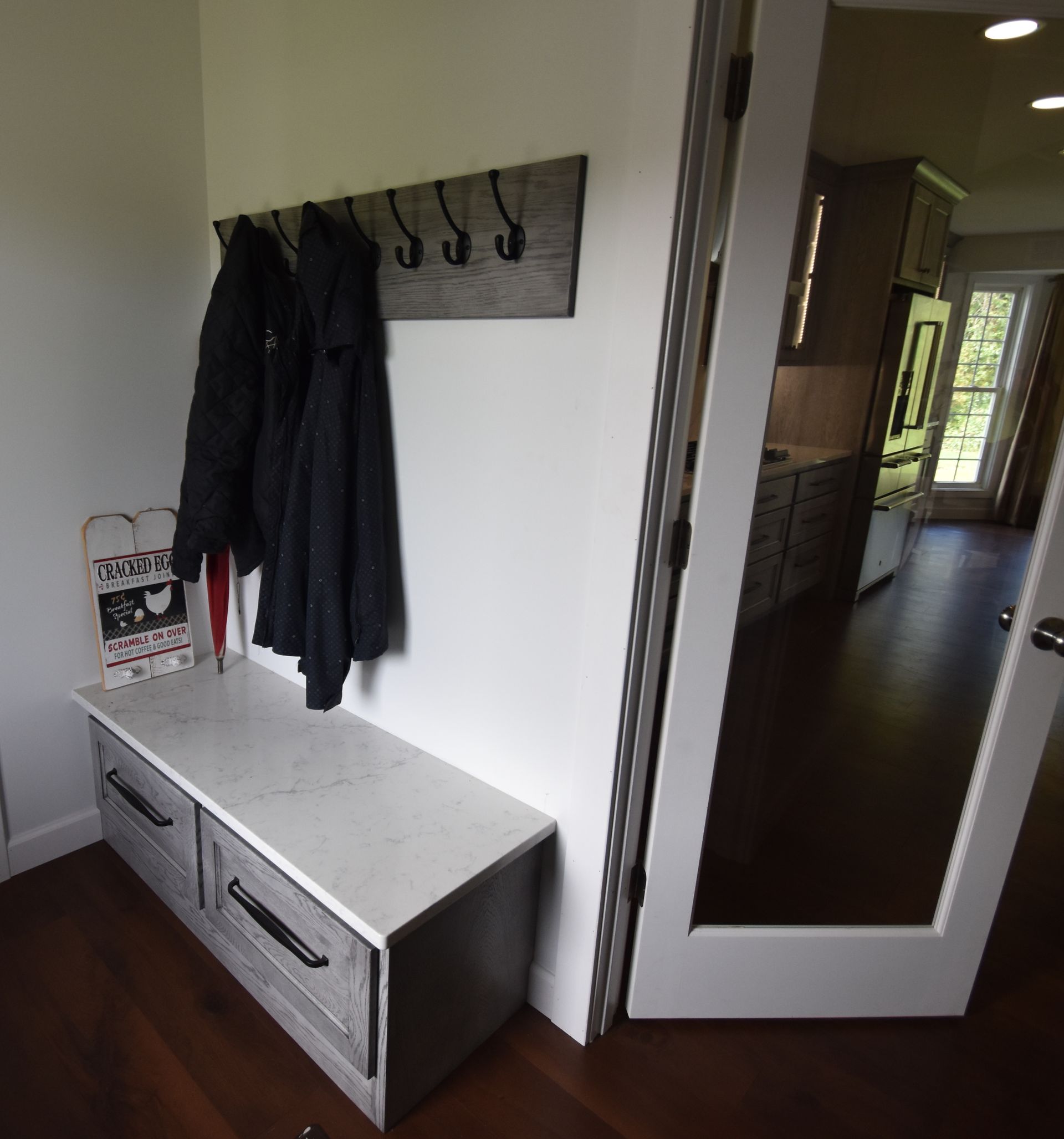 Entryway with coat rack, bench, and a full-length mirror beside a hallway.